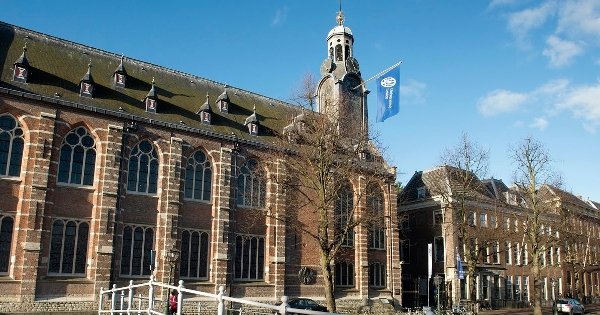 Historic brick church with arched windows, a tower, and a flag, under a clear blue sky.