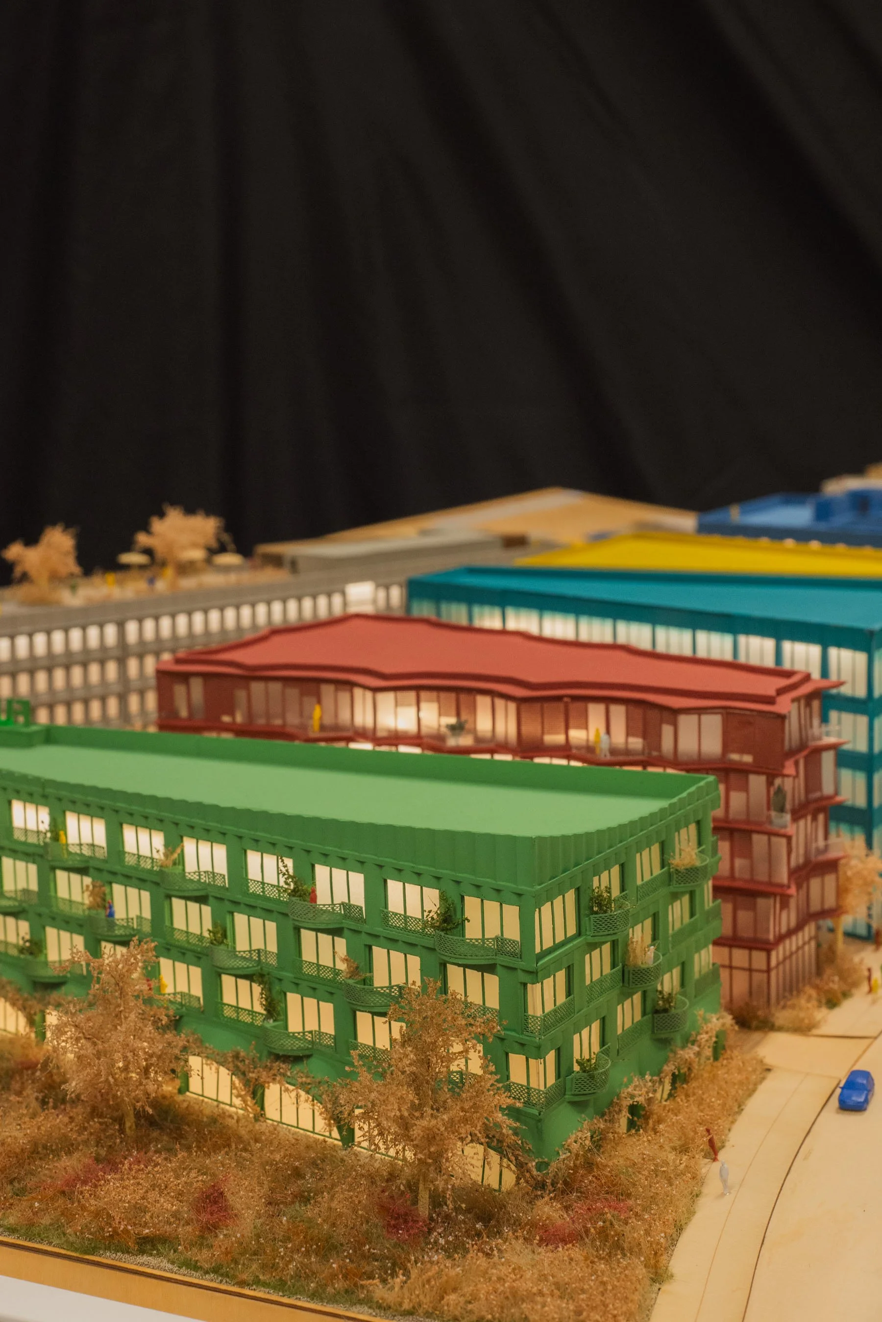 Model of colorful multi-story buildings in an urban neighborhood, with trees and a sidewalk and street in front.
