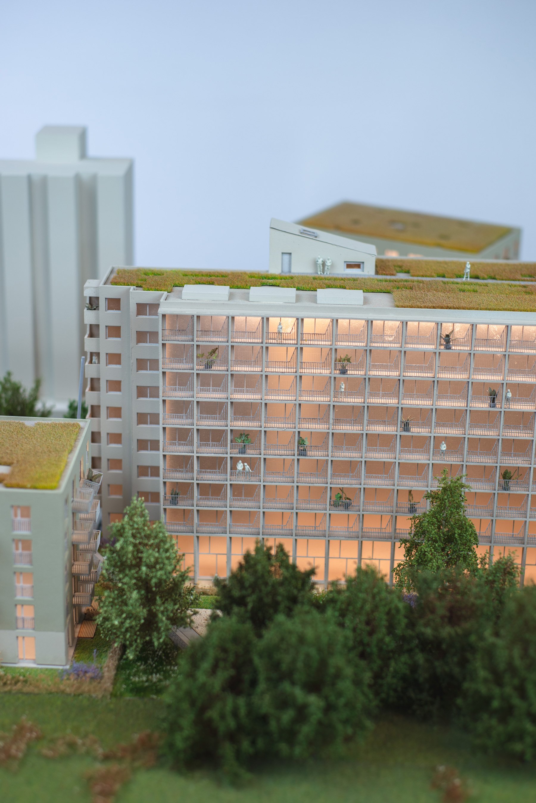 A detailed architectural model of a modern multi-story residential building with a green rooftop garden, small figures of people, in a natural setting with trees.