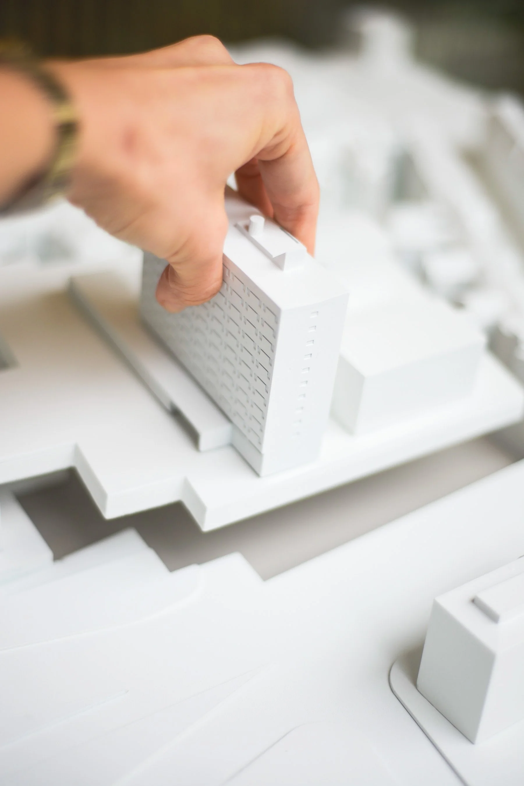 Close-up view of a hand adjusting a white architectural model of a building with a highlighted rooftop area.