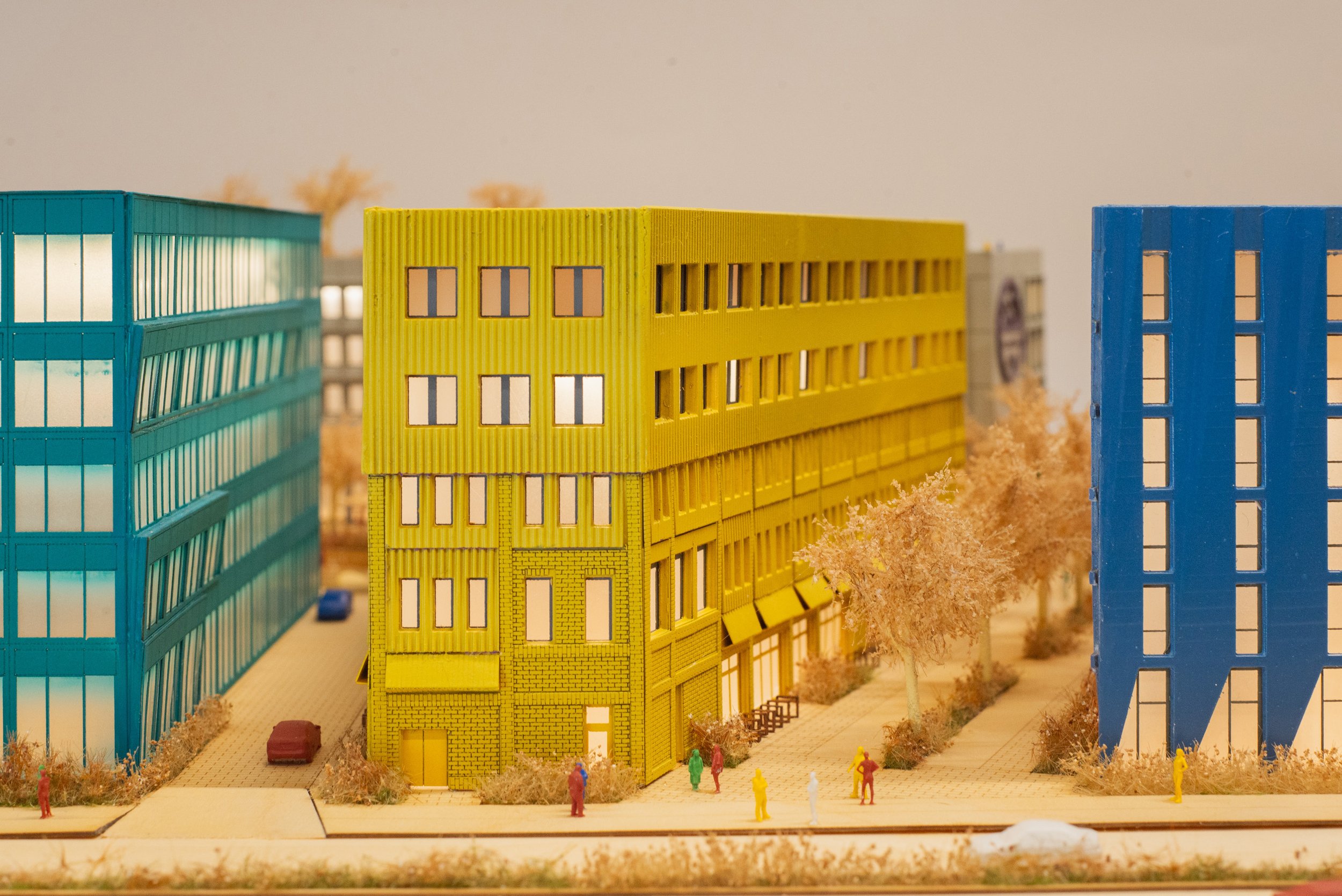A miniature model of a city street with colorful buildings, trees, cars, and tiny people.