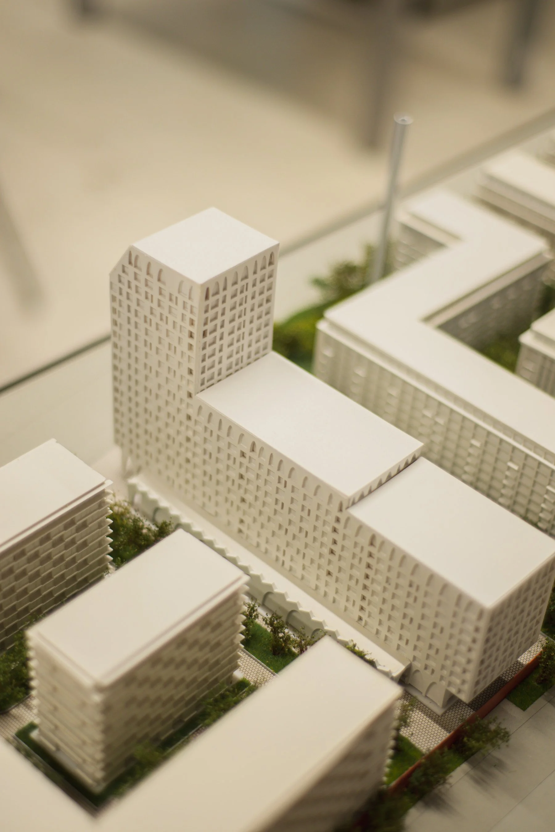 A miniature architectural model of a modern city with white high-rise buildings, some with grid-like windows, and green trees, viewed from an angle.