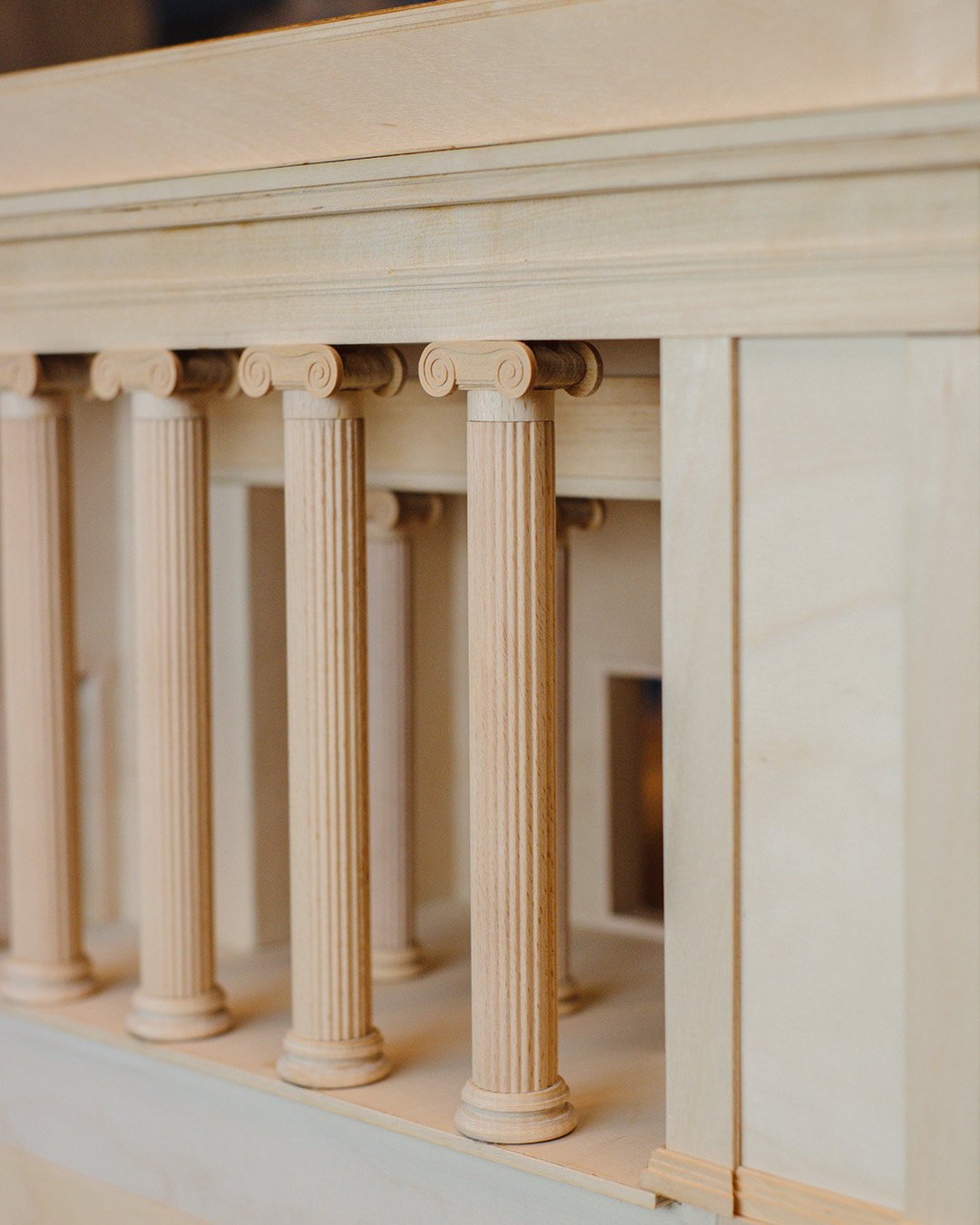 Close-up of a miniature wooden structure with vertically aligned columns and detailed capitals resembling classical architectural style.
