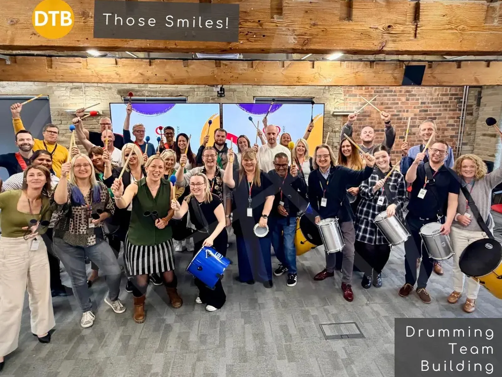 Large group of colleagues smiling and holding up drumsticks after a samba drumming session