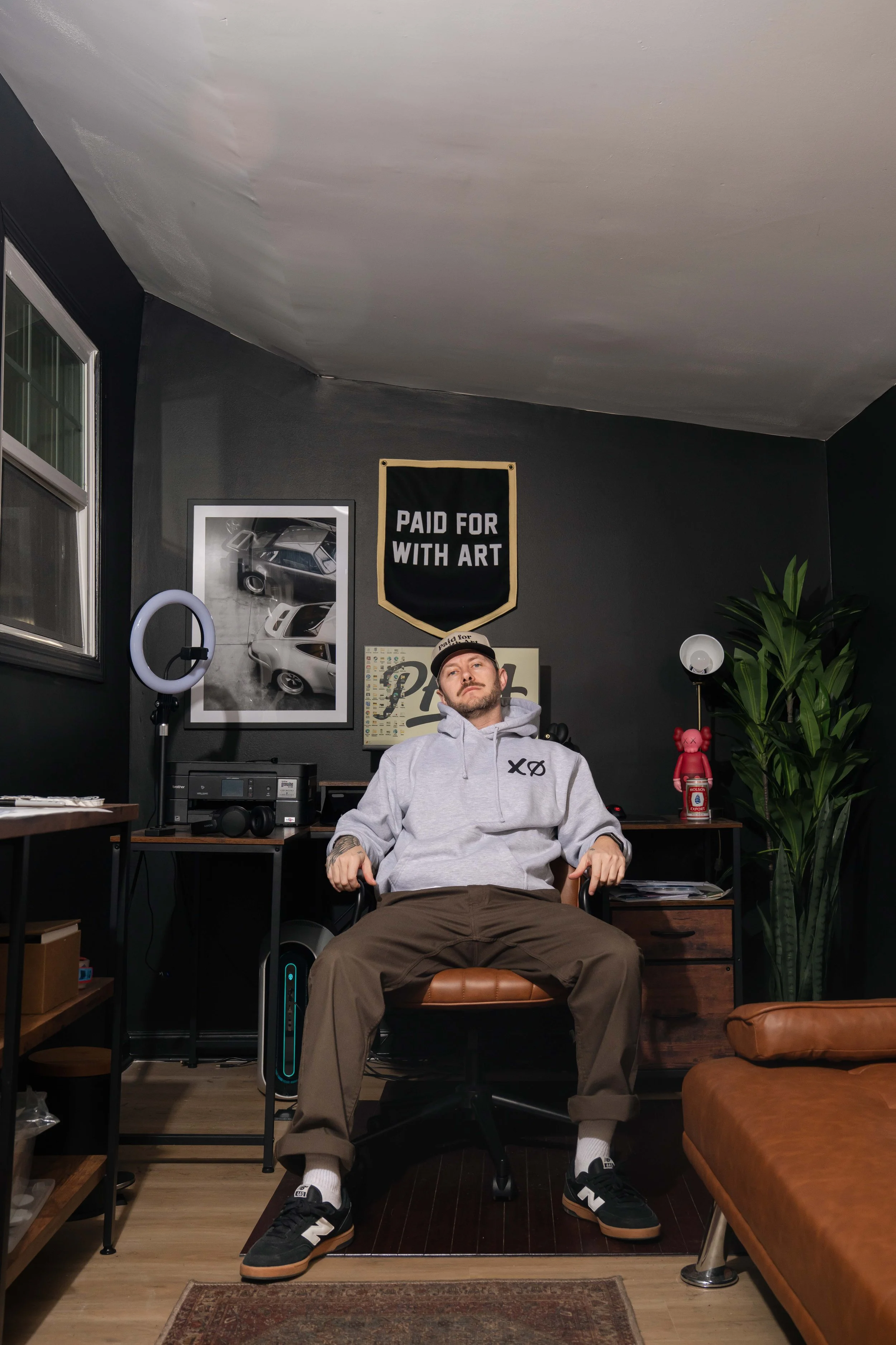 Founder of Paid For With Art seated in his home studio beneath the PFWA banner