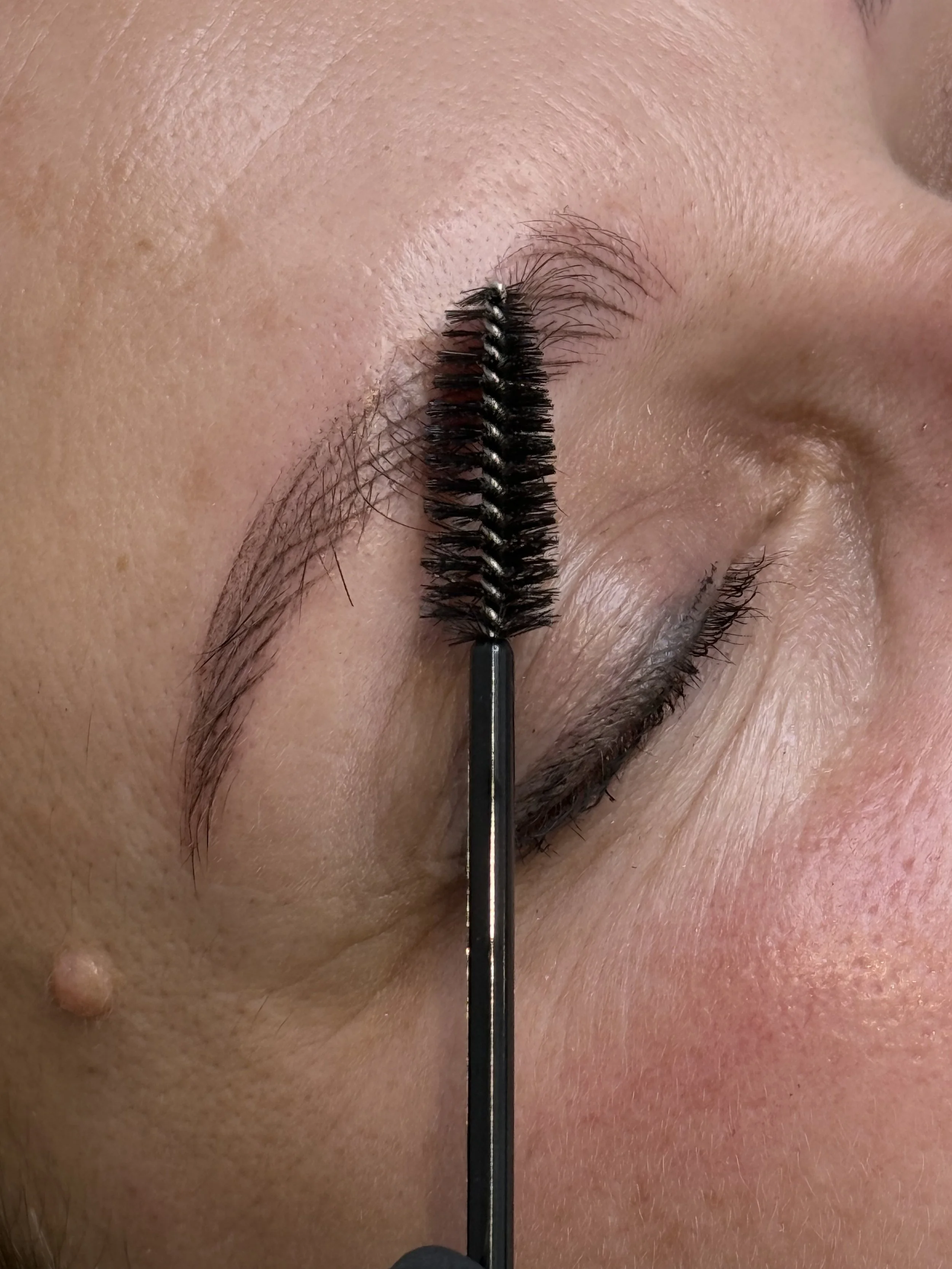 Nano Brows | Hyper-realism Brows Cambridge — Close-up image of a person's eye with an eyelash brush applying mascara  — Cambridge Brow Sanctuary