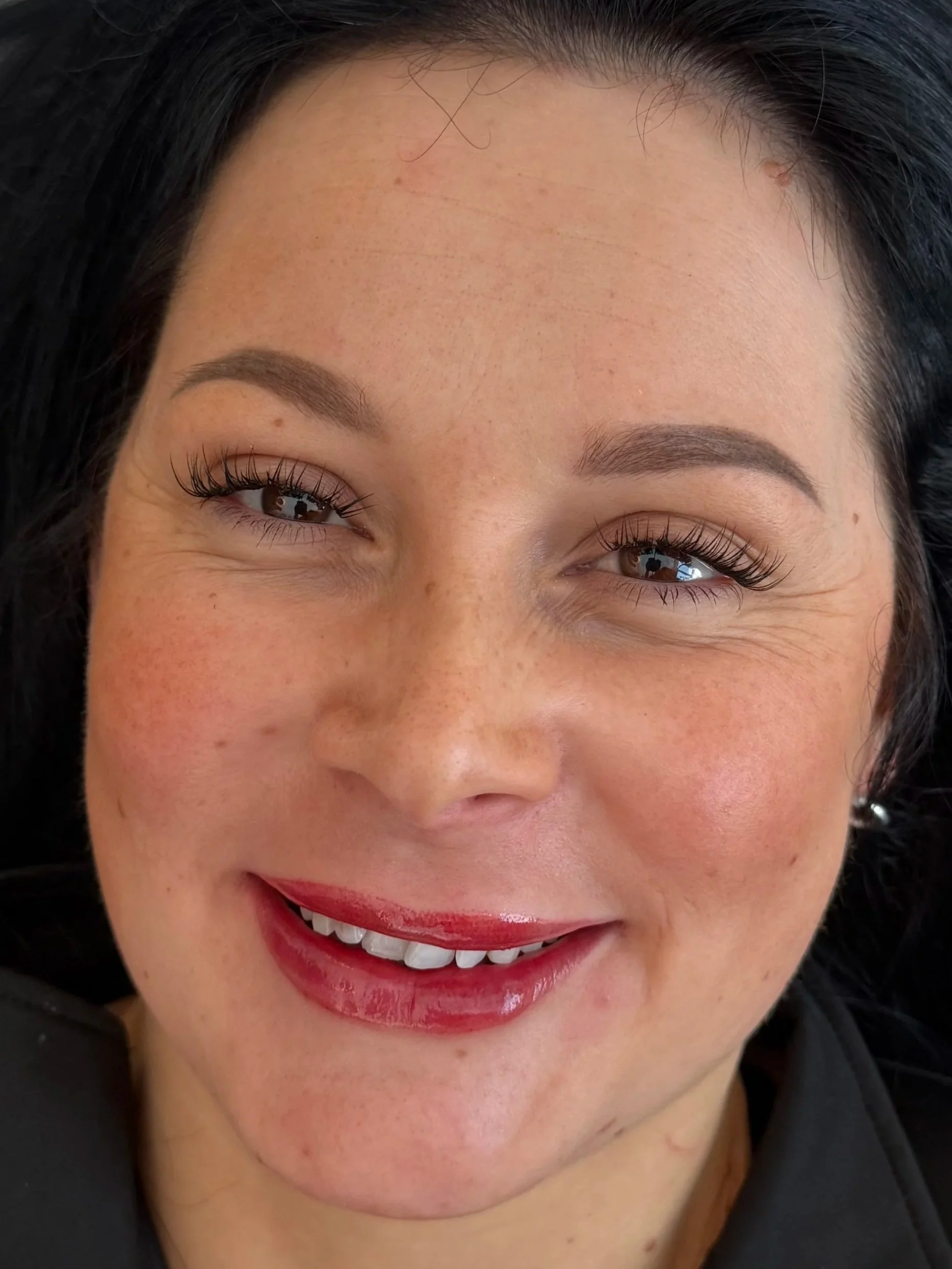 Lip Blush Cambridge — Close-up of a woman's smiling face showing her eyes, eyebrows, nose, and mouth with red lipstick  — Cambridge Brow Sanctuary
