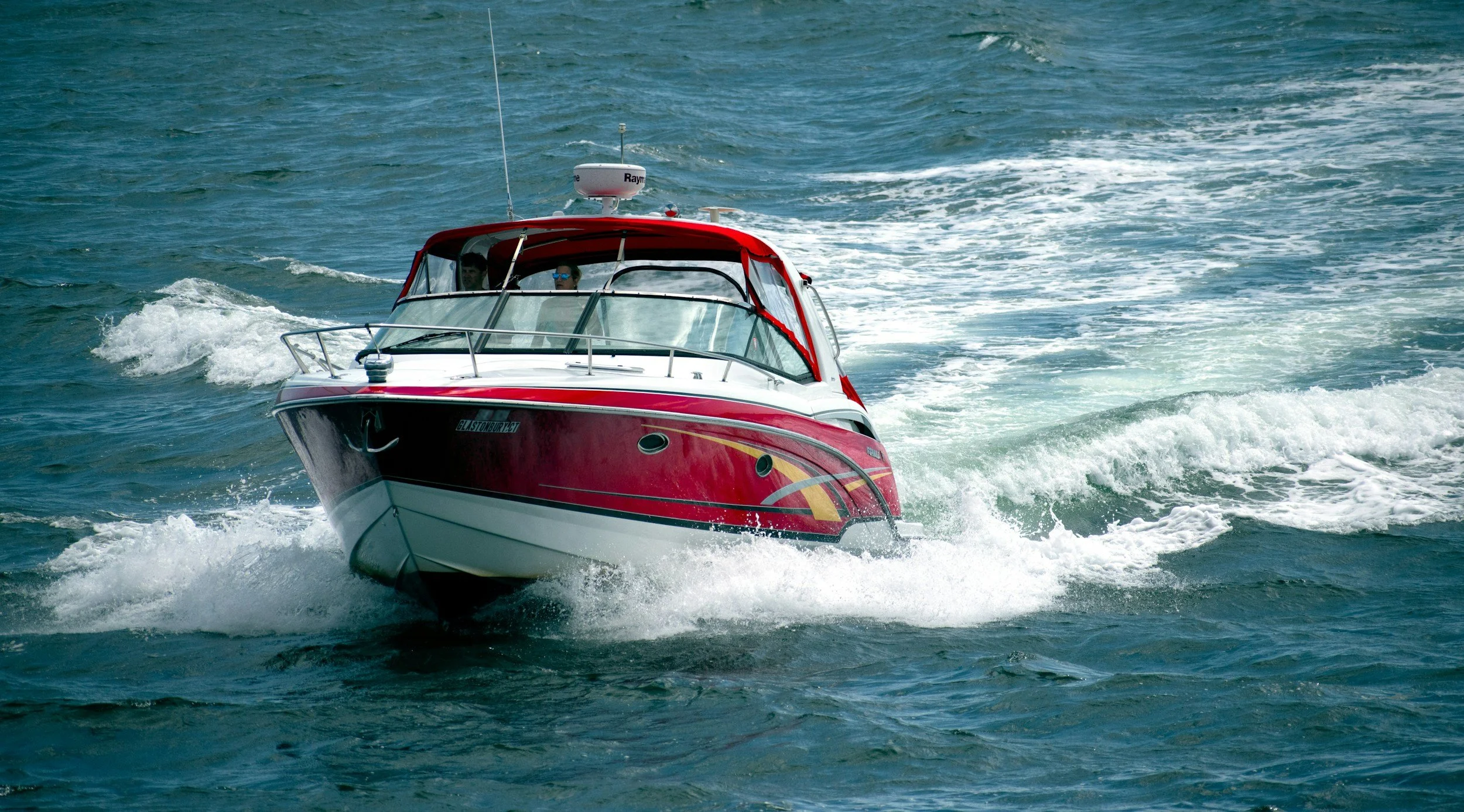 A red and white motorboat speeding through the water, creating a wake behind it.