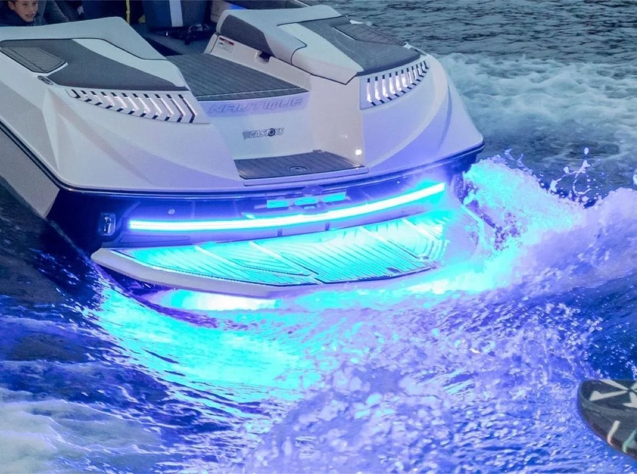 A luxury speedboat with blue LED lights illuminating its front, moving through the water at night, creating waves.