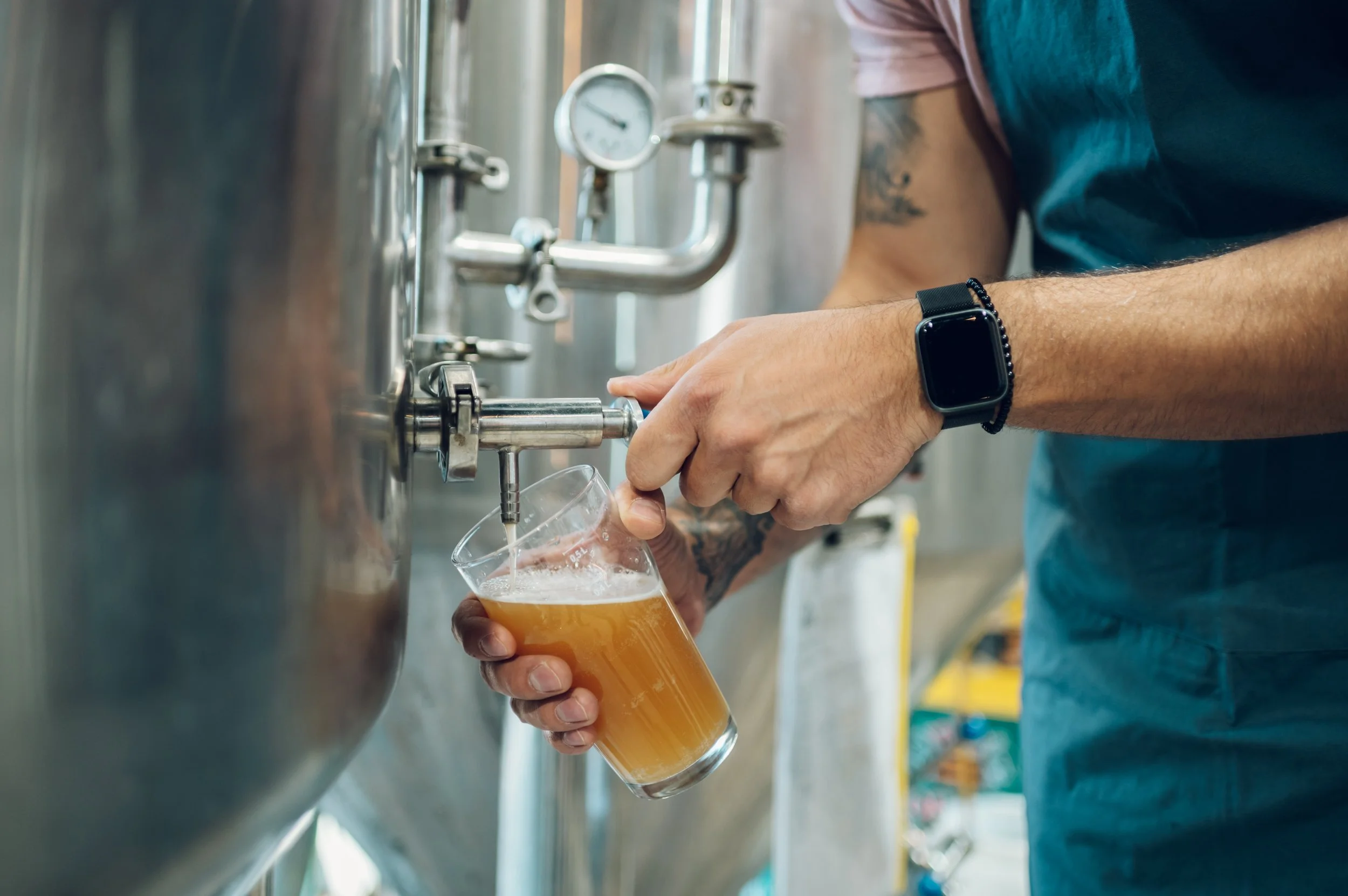 Person pouring beer from a tap into a glass in a brewery setting.