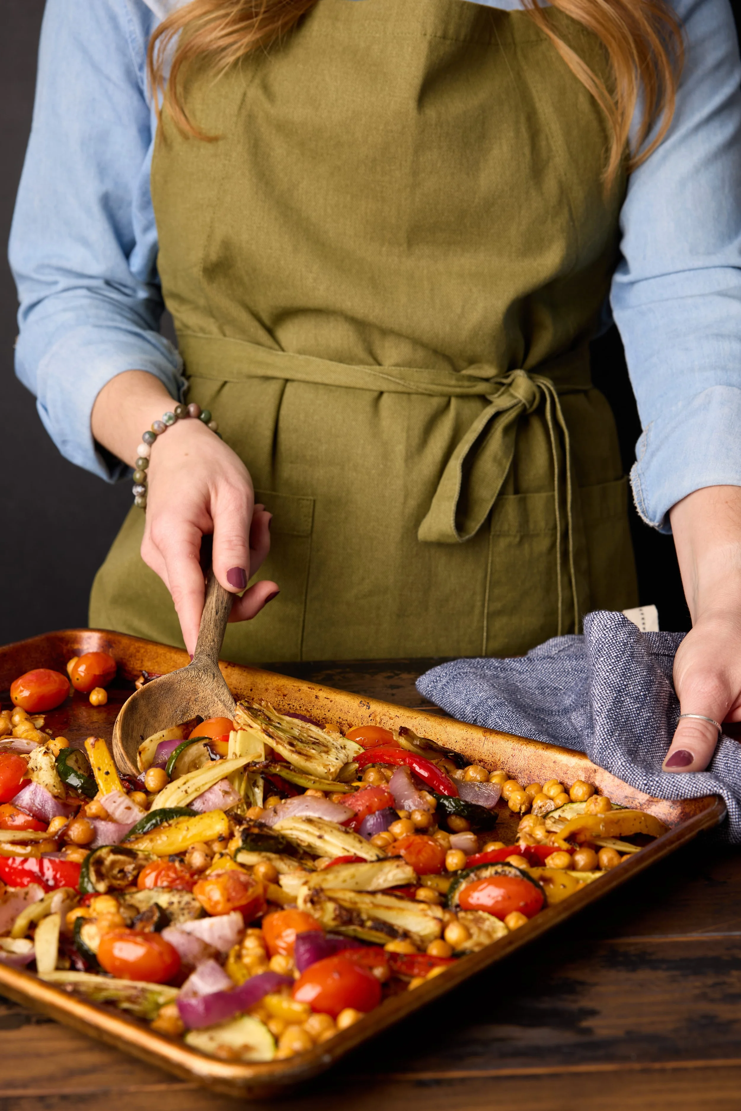 woman wearing a green apron serving chickpea ratatouille from a sheet pan