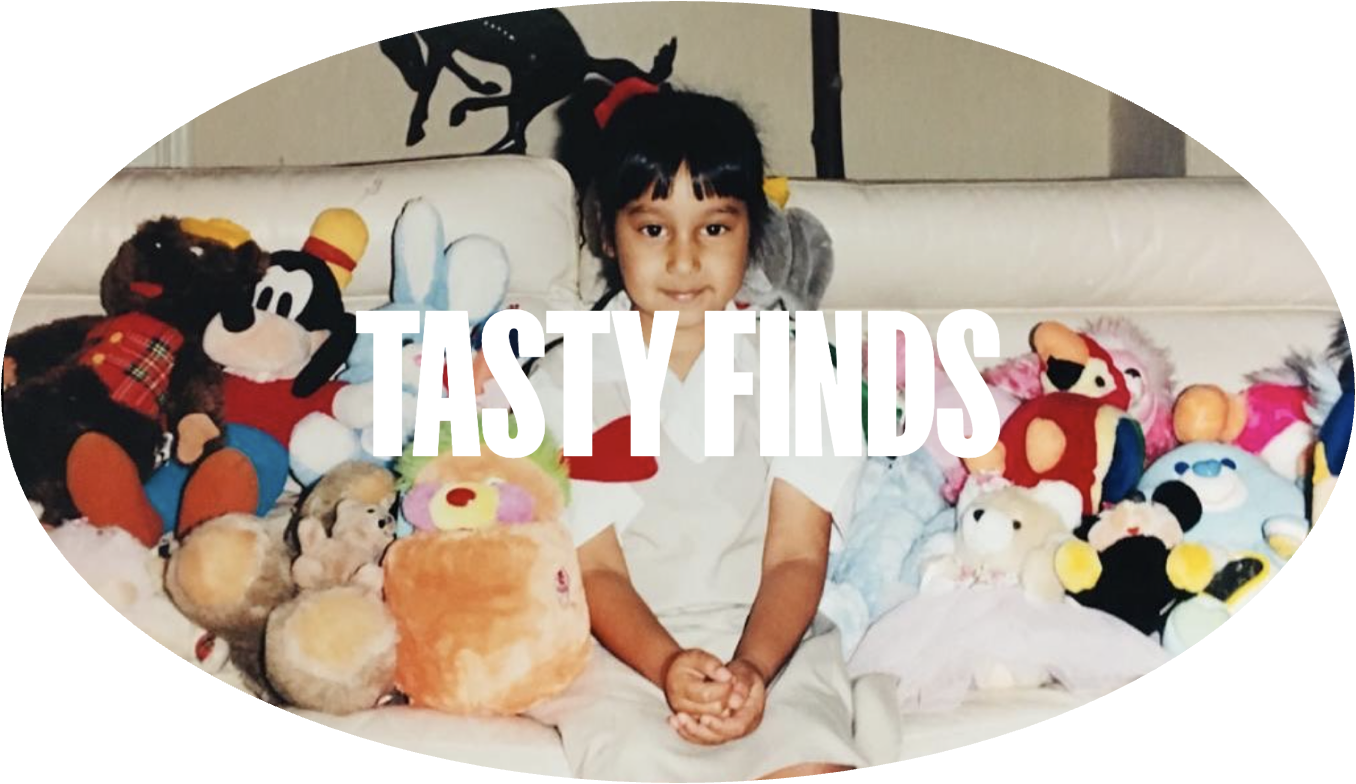 A young girl sitting on a cream-colored couch surrounded by plush toys, with white text 'TASTY FINDS' overlayed on the image.