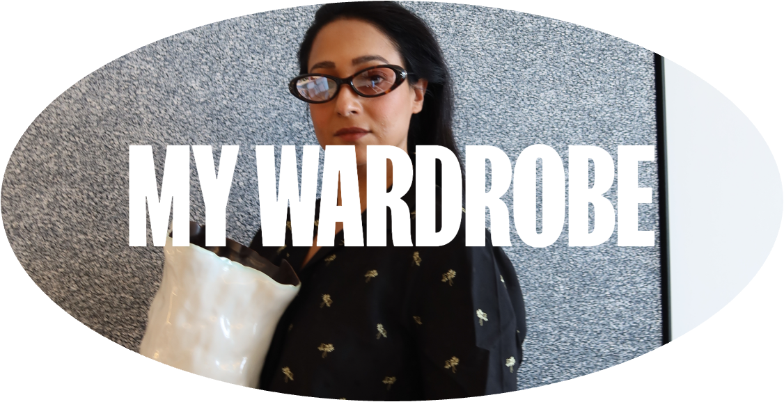 A woman with dark hair and glasses holding a white handbag, standing in front of a gray textured wall with a partial curving shape, and a whiteboard or screen on the right side, with the text "MY WARDROBE" overlaid.