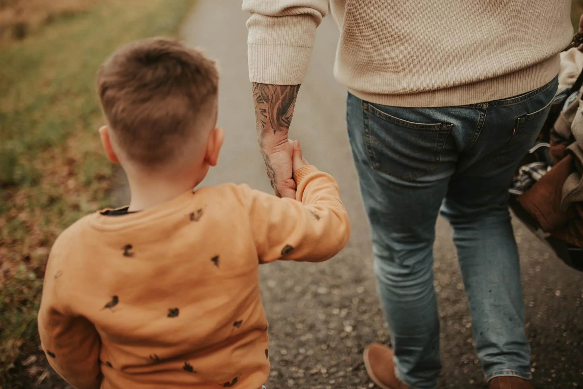 Een kind houdt de hand vast van een volwassene terwijl ze samen wandelen op een pad, met namen op de lange mouwen van het kind.