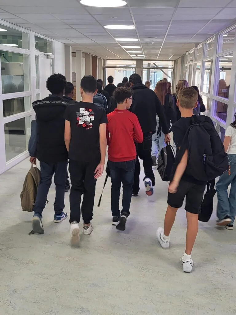 Groep jongeren loopt door een schoolgang met veel ramen en plafondlichten.