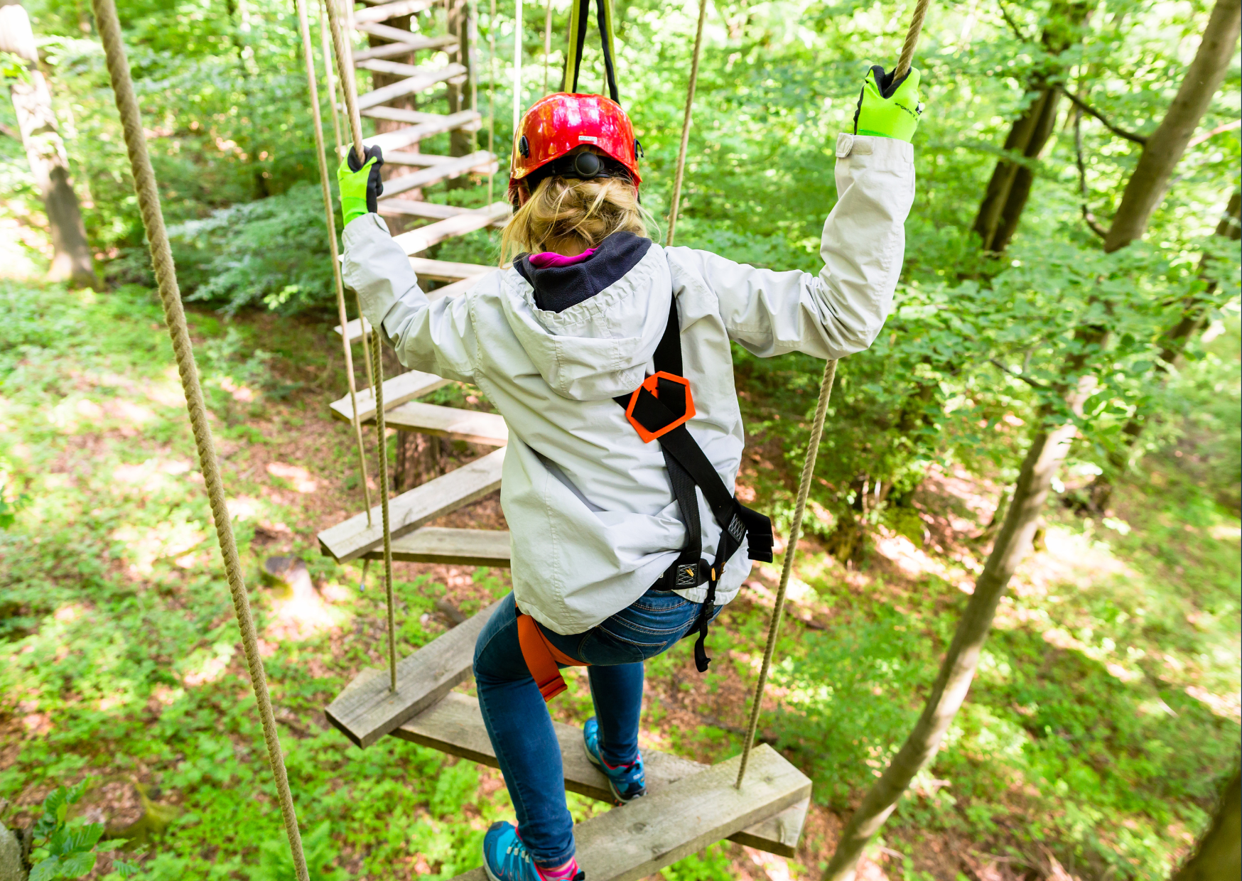 Persoon veilig gekleed met een helm en handschoenen die een touw vasthoudt tijdens een touwenparcours in het bos.