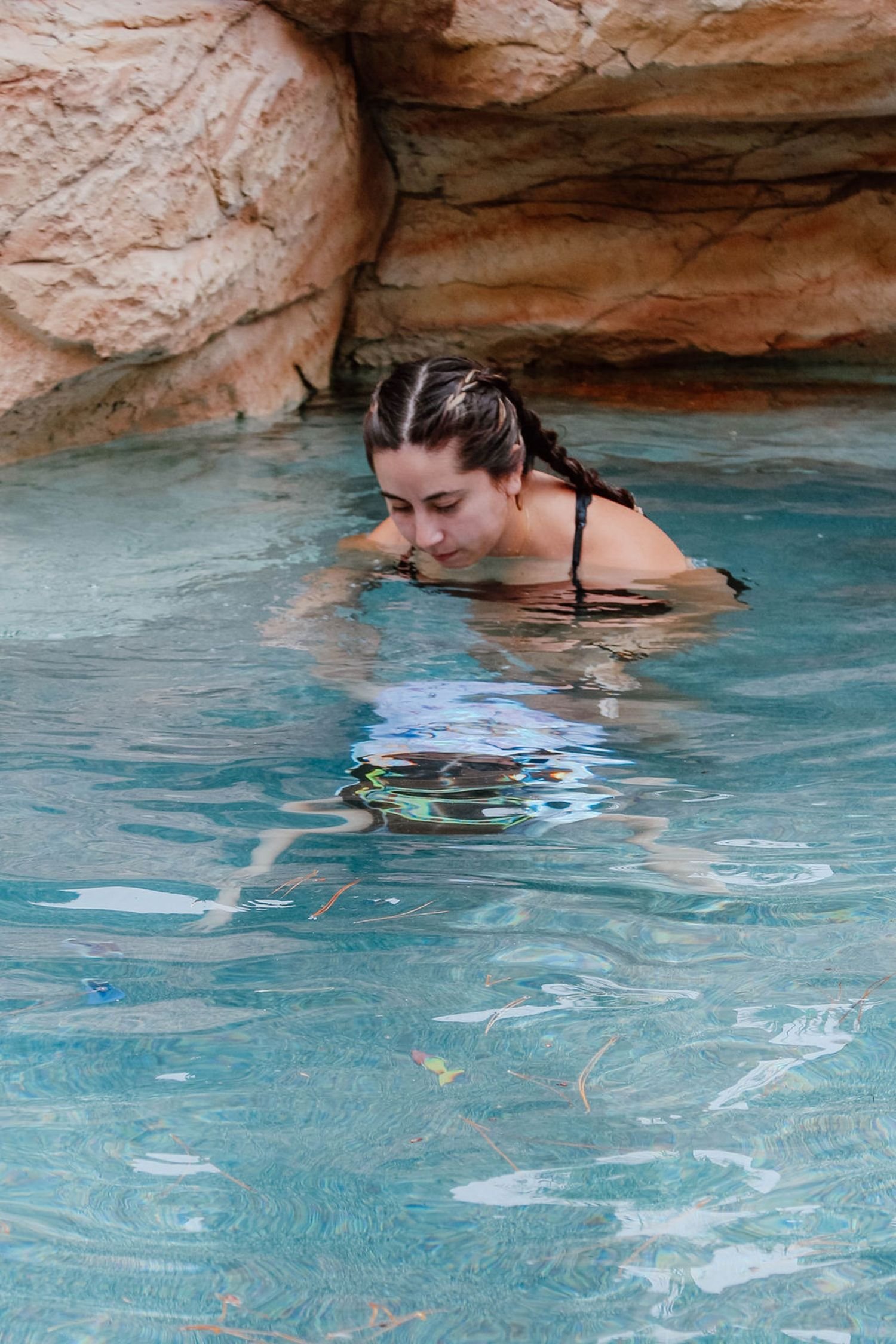 Woman with braided hair in black swimsuit leaning into a clear, blue body of water with rocks in the background.  Survival Swim Lessons