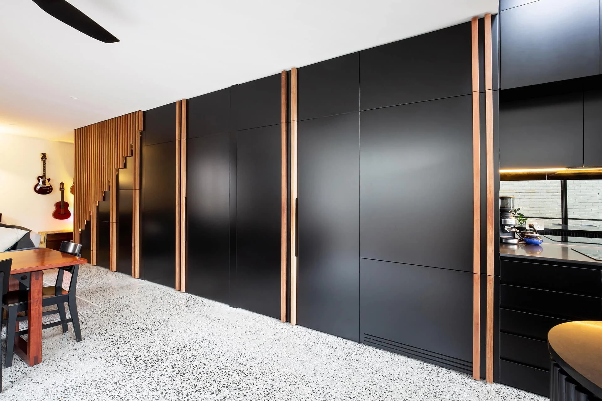Modern black kitchen with wooden accents, partial view of dining area, and a partition wall separating the kitchen from the living space.