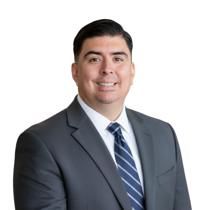 A professional man in a dark suit, white shirt, and blue striped tie. He has short dark hair and is smiling. The background is plain black.