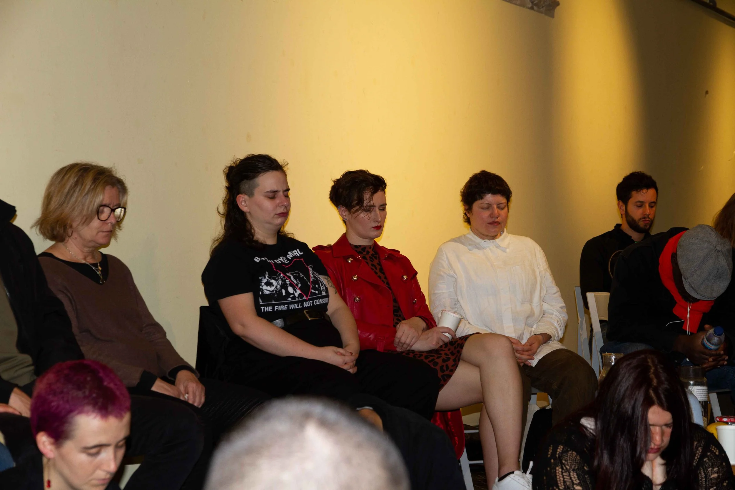 Group of people sitting with eyes closed during a meeting or meditation session, diverse ages and styles.