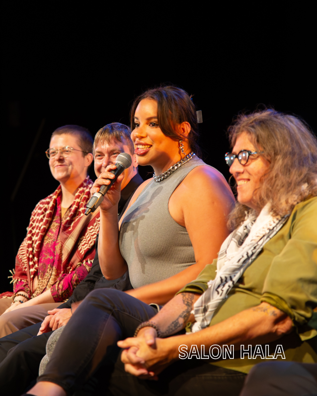 A group of five people sitting on stage at a panel discussion or event, with one woman speaking into a microphone. The background is black, and the words 'SALON HALA' are written in white at the bottom right of the image.