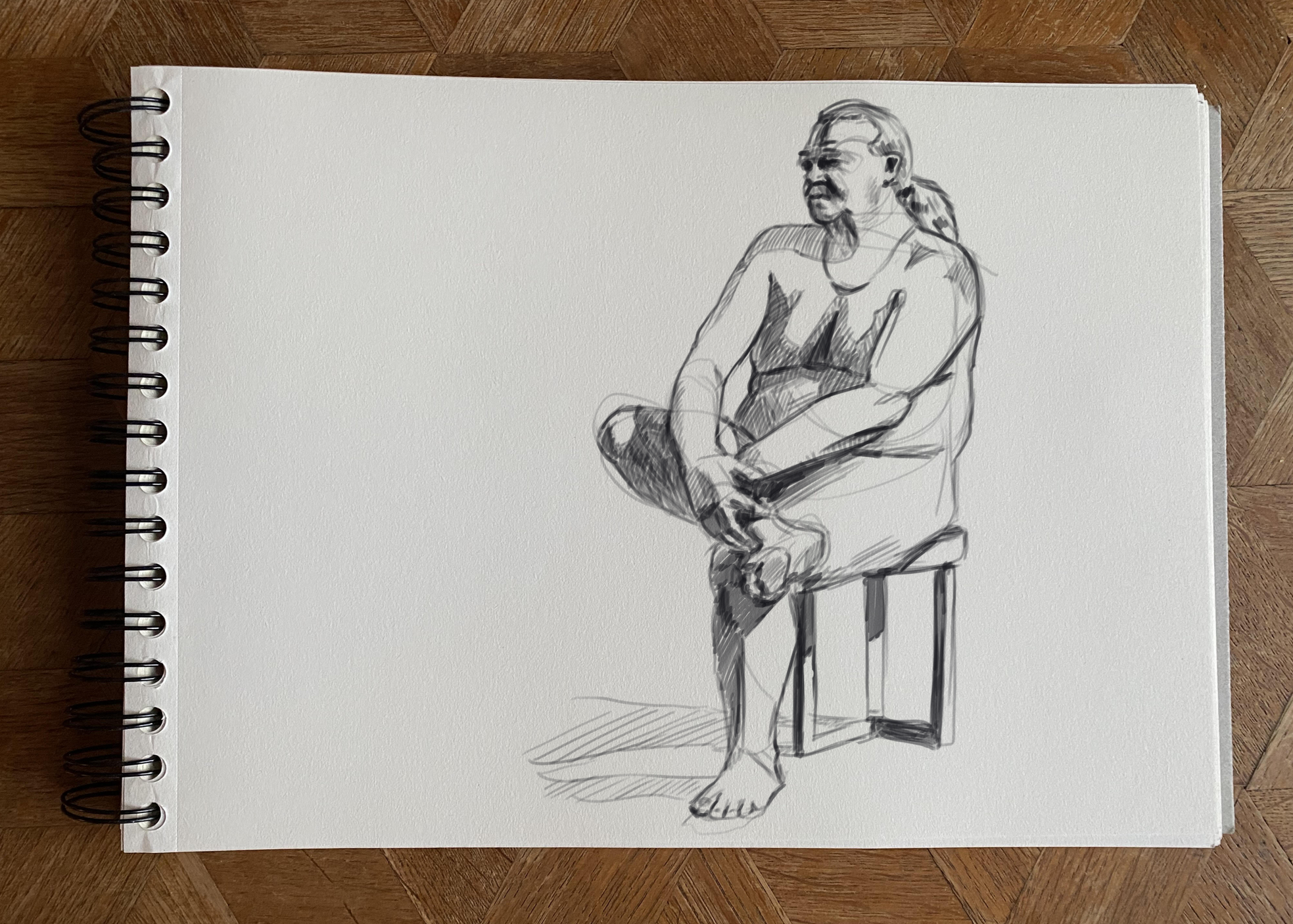 Sketch of a woman sitting on a stool with one leg crossed over the other, looking to the side, on a white textured paper.