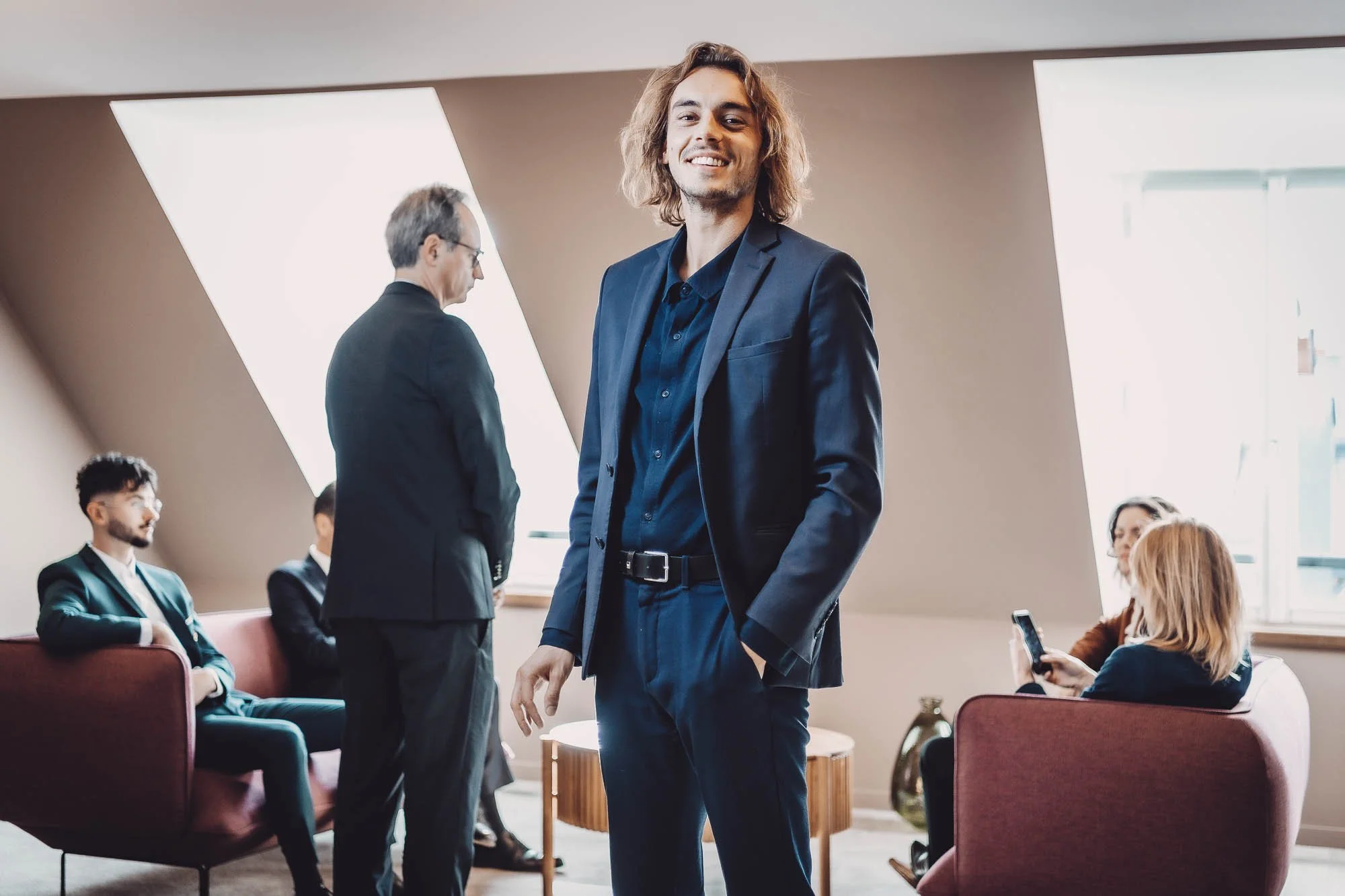 Groupe de personnes en tenue professionnelle discutant et utilisant leurs téléphones dans un bureau moderne.