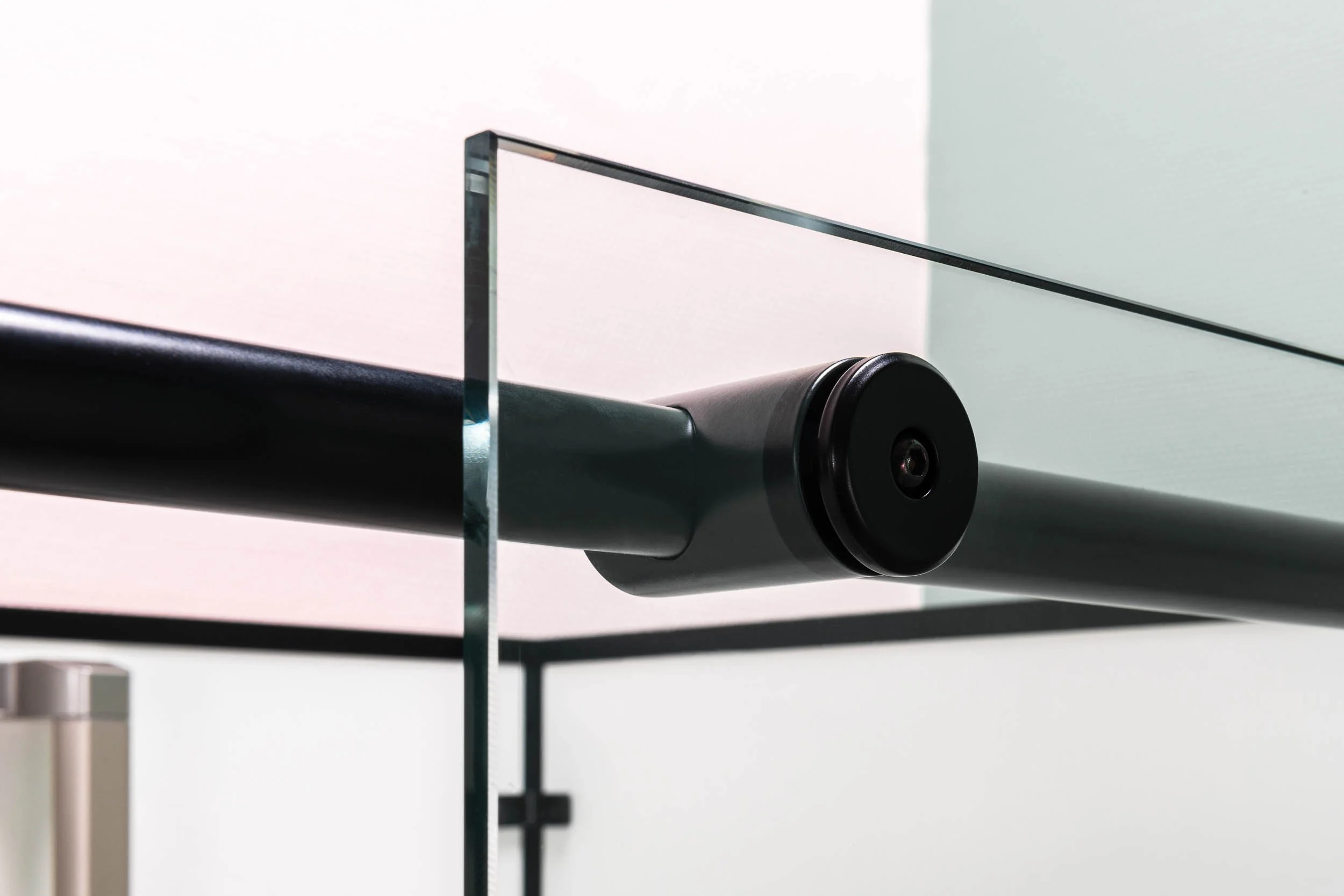 Détail d'un raccord en métal noir sur une paroi de verre, probablement une cabine de douche.