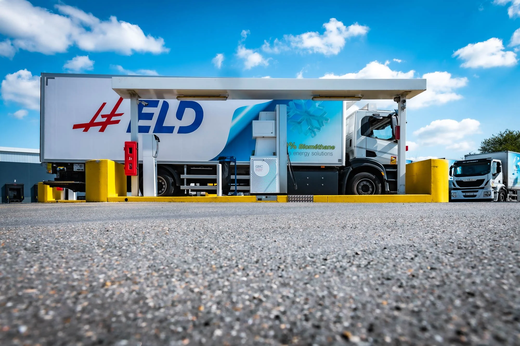 Camion au stationnement d'une station-service de GNC sous un ciel bleu.