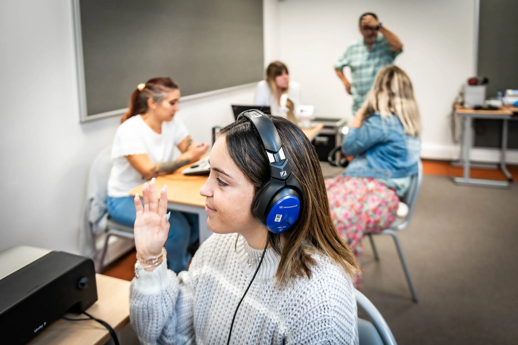 Groupe de personnes dans une salle, individus portant des écouteurs, travaillant sur des ordinateurs ou appareils électroniques.