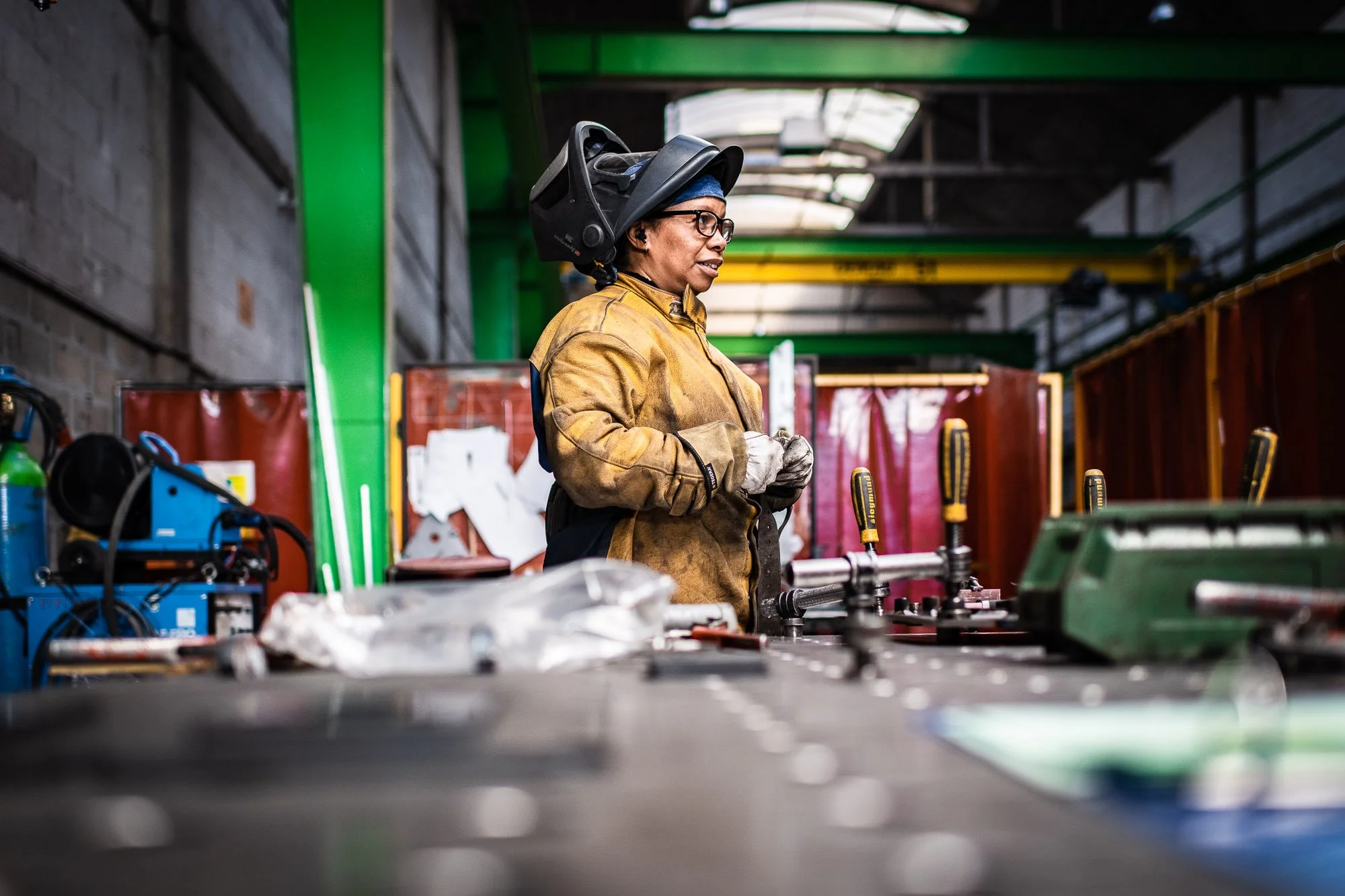 Une personne portant un équipement de protection se tient dans un atelier industriel devant une table avec des outils.