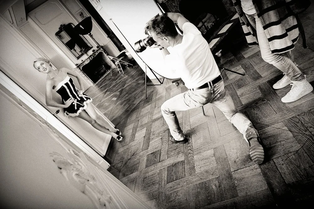 Un photographe prenant une photo d'une femme en tenue de scène dans un studio avec un plancher en bois.
