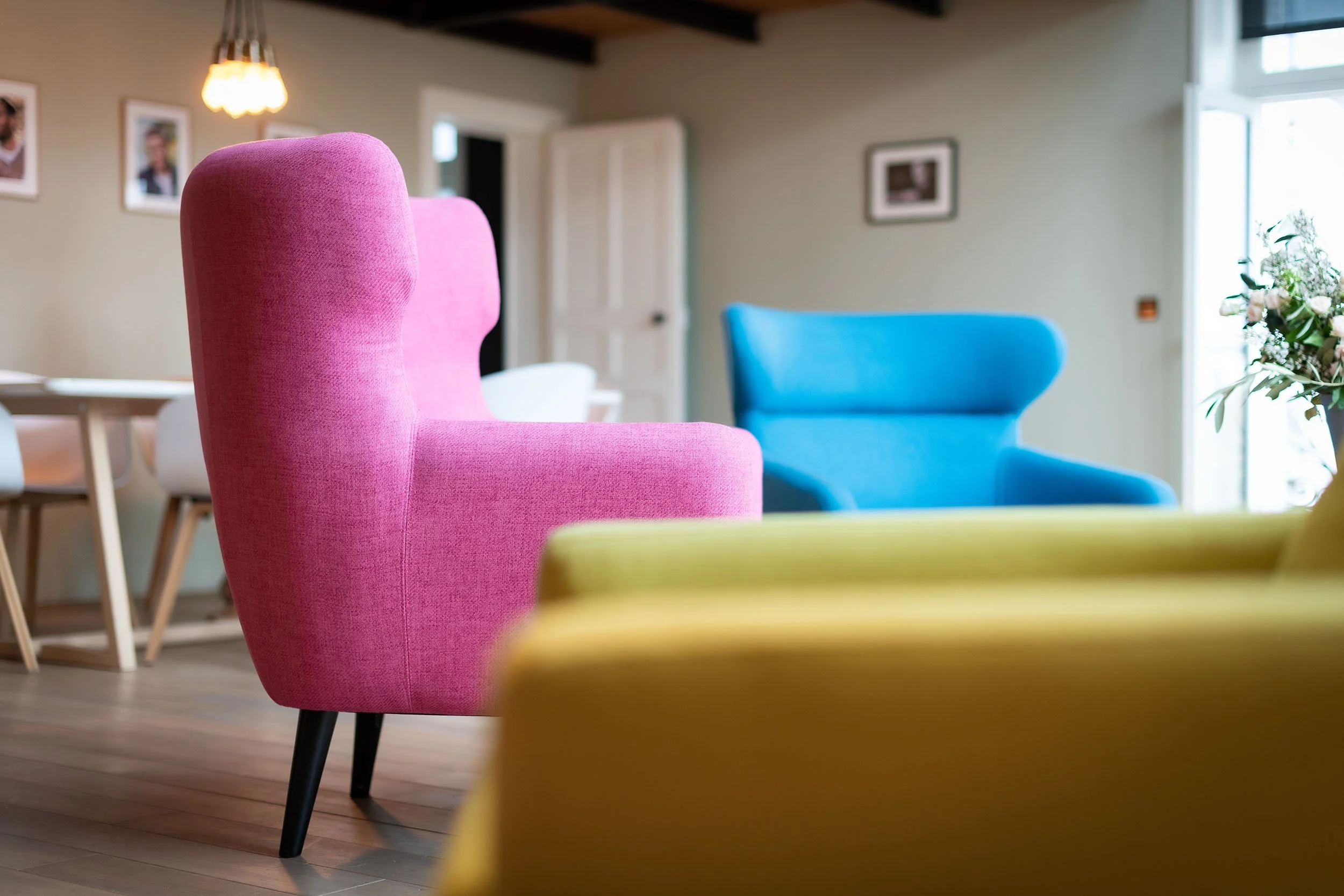 Fauteuils colorés dans une salle moderne avec des cadres au mur et une lampe suspendue.