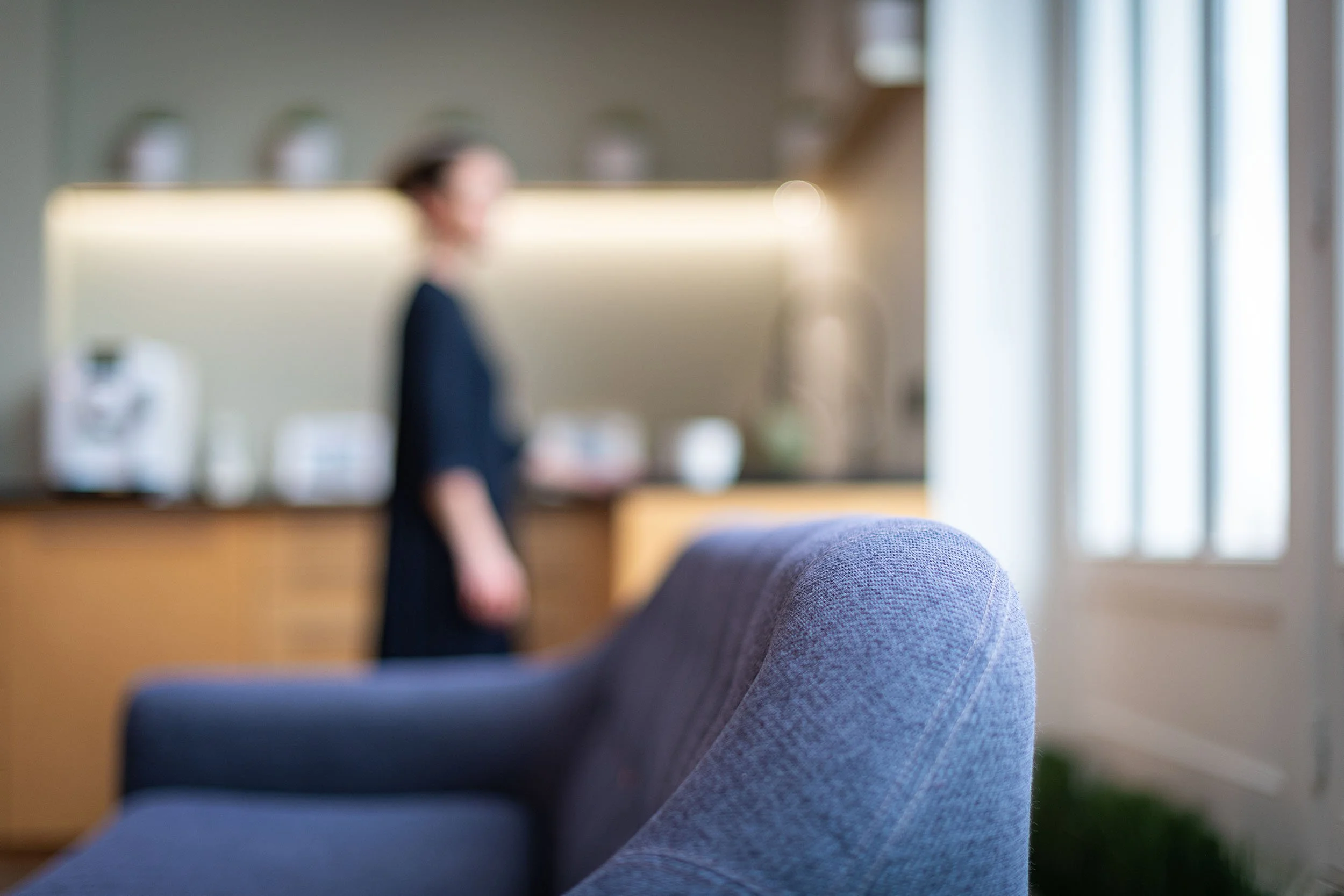 Intérieur flou avec une personne debout près d'un canapé gris dans la cuisine.