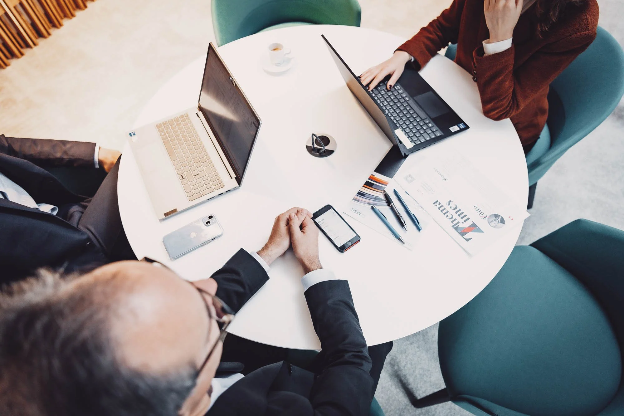 Réunion de travail avec deux personnes utilisant des ordinateurs portables autour d'une table, avec des documents et un smartphone.