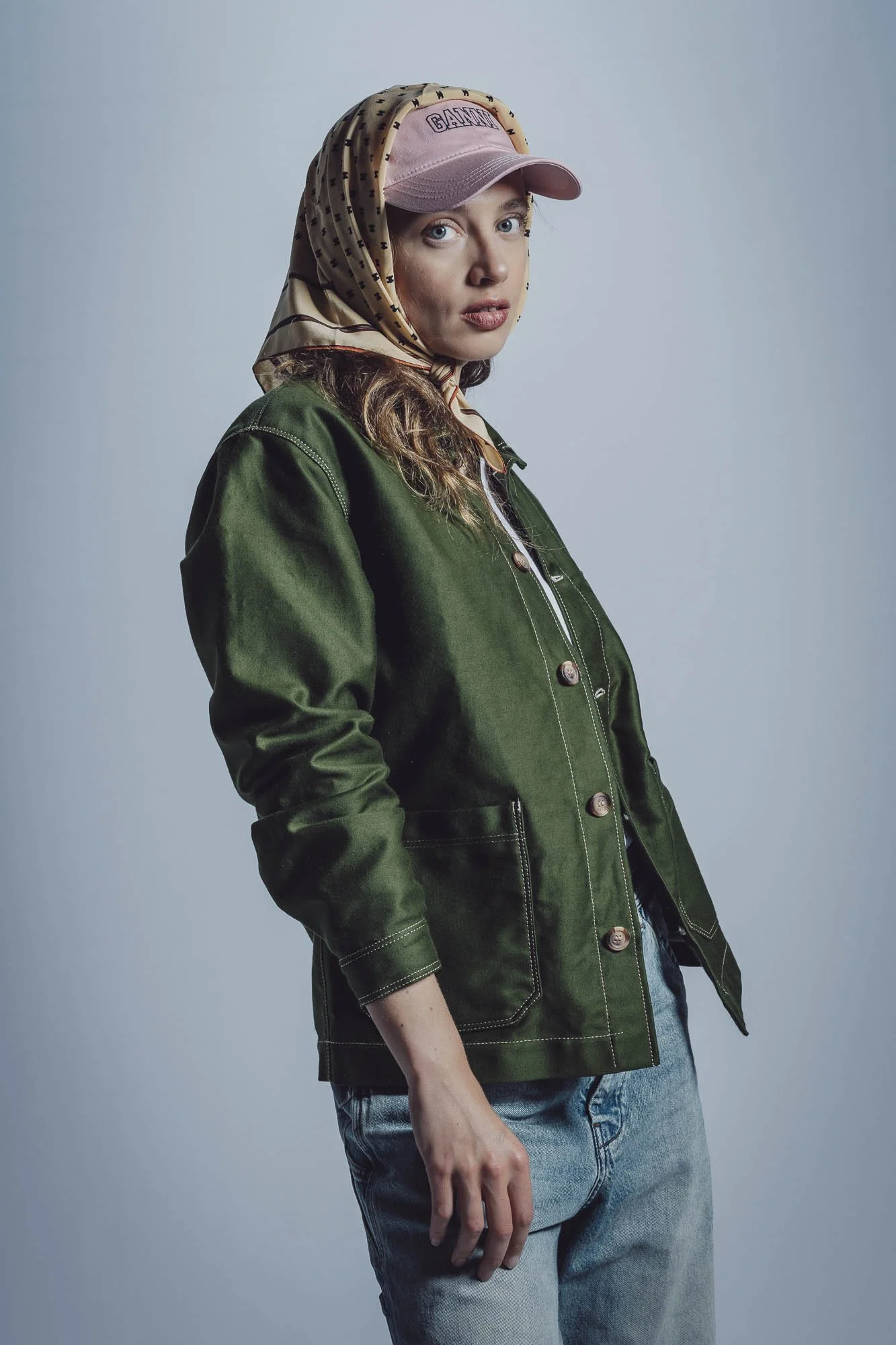 Une personne portant une casquette rose et un foulard, avec une veste verte et un jean.