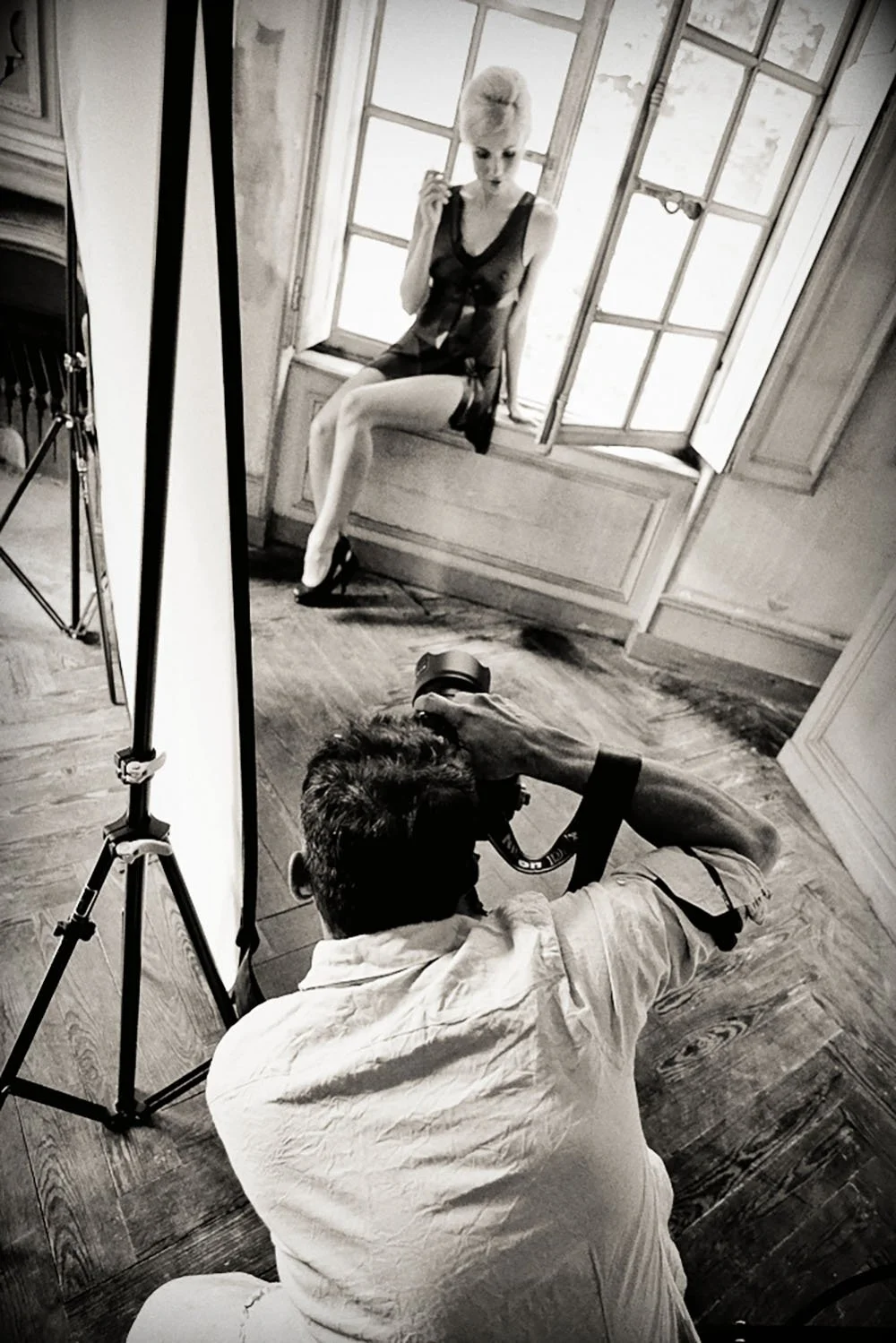 Photographe prenant une photo d'une femme assise sur un rebord de fenêtre, éclairage professionnel installé.