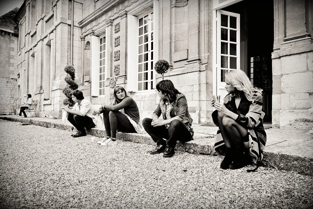 Groupe de personnes assises devant un bâtiment en pierre, discutant et relaxant.