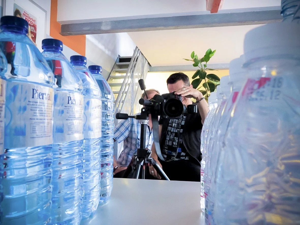 Un photographe prenant des photos entre des rangées de bouteilles d'eau en plastique sur une table.