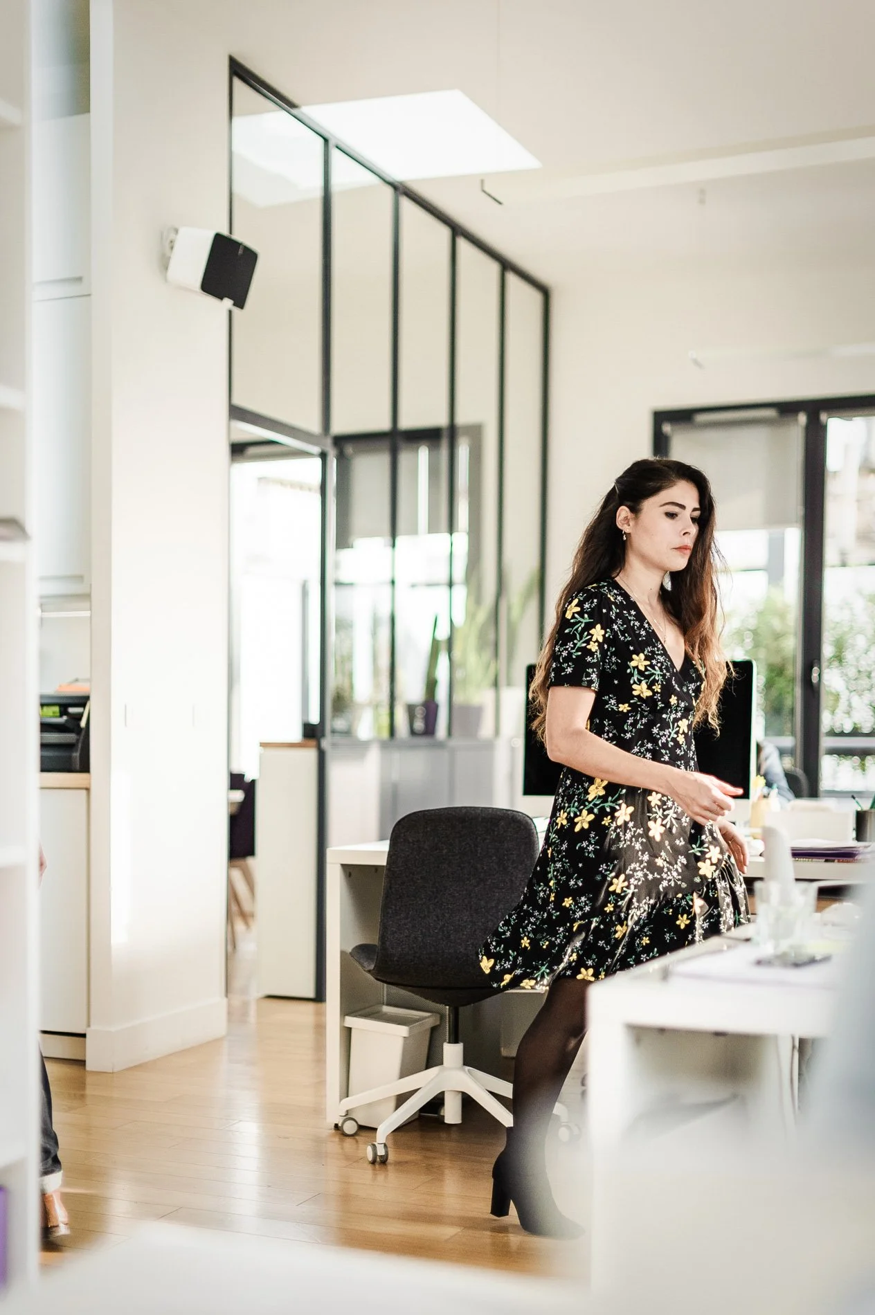 Femme en robe fleurie marchant dans un bureau moderne et lumineux.