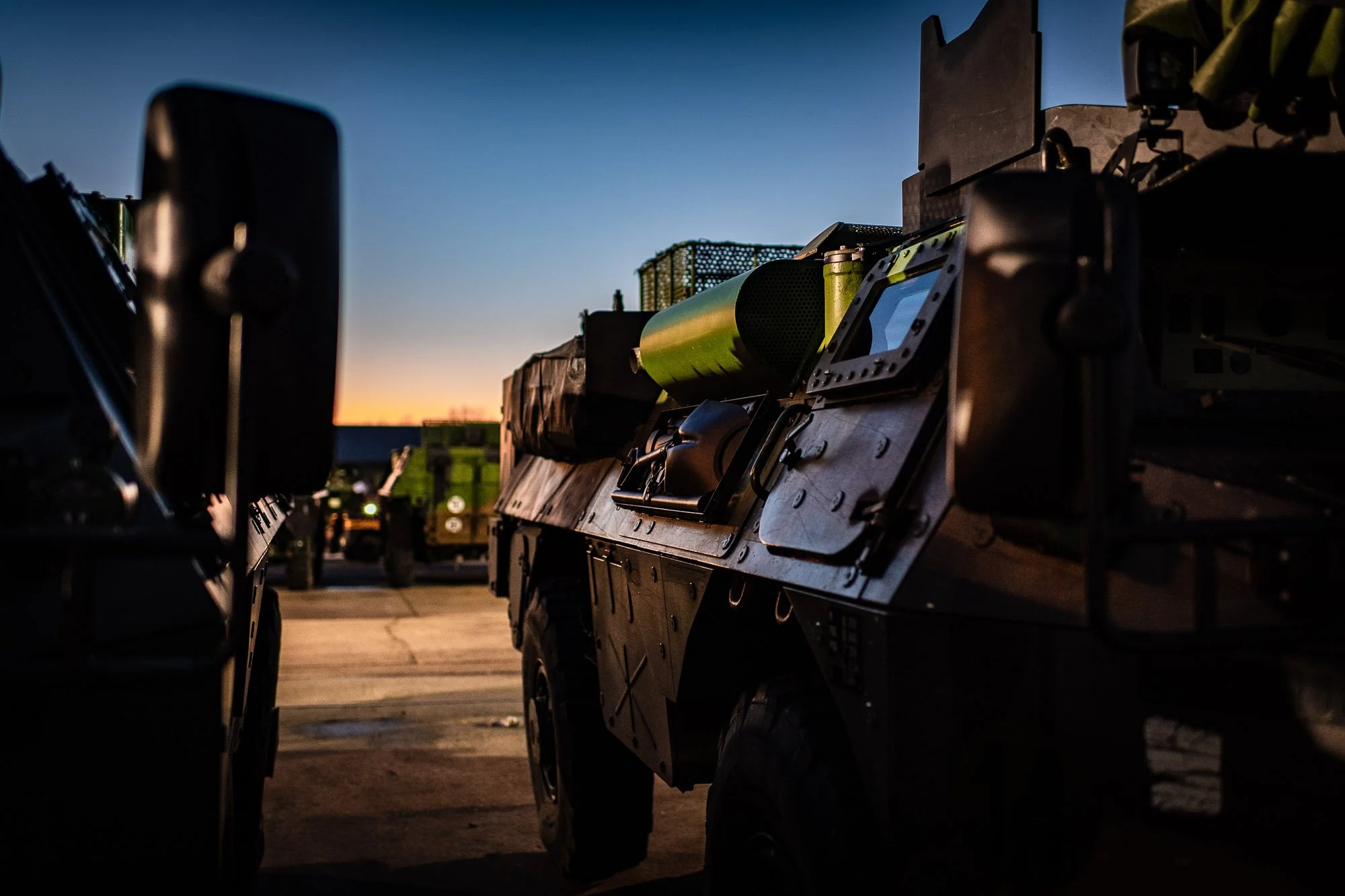 Véhicules militaires alignés au coucher du soleil sur une base.