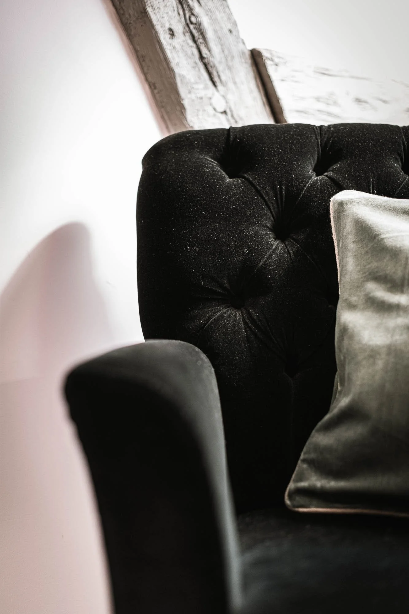 Fauteuil noir en velours avec coussin, contre un mur blanc