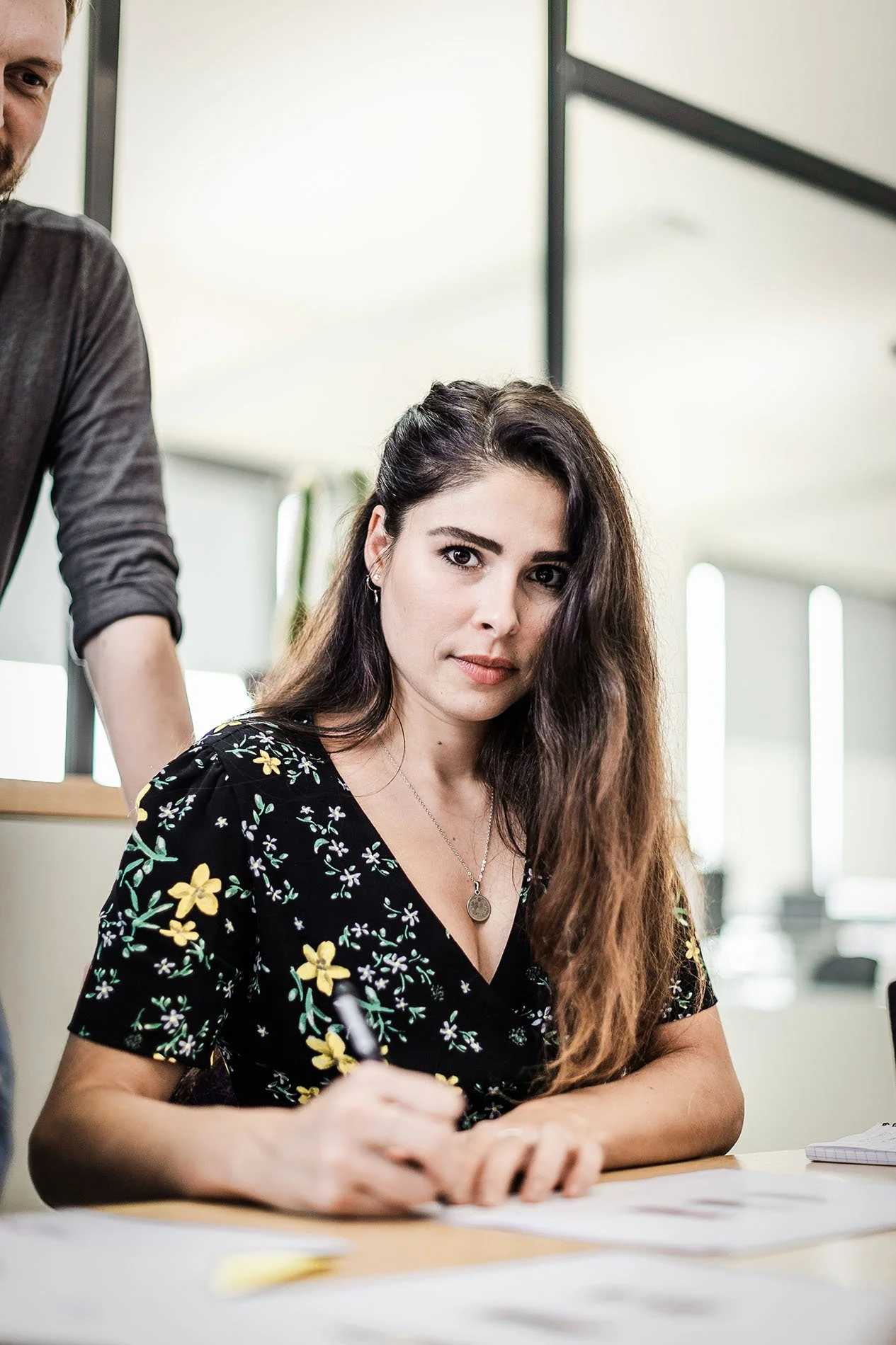 Femme en robe fleurie écrivant à un bureau.