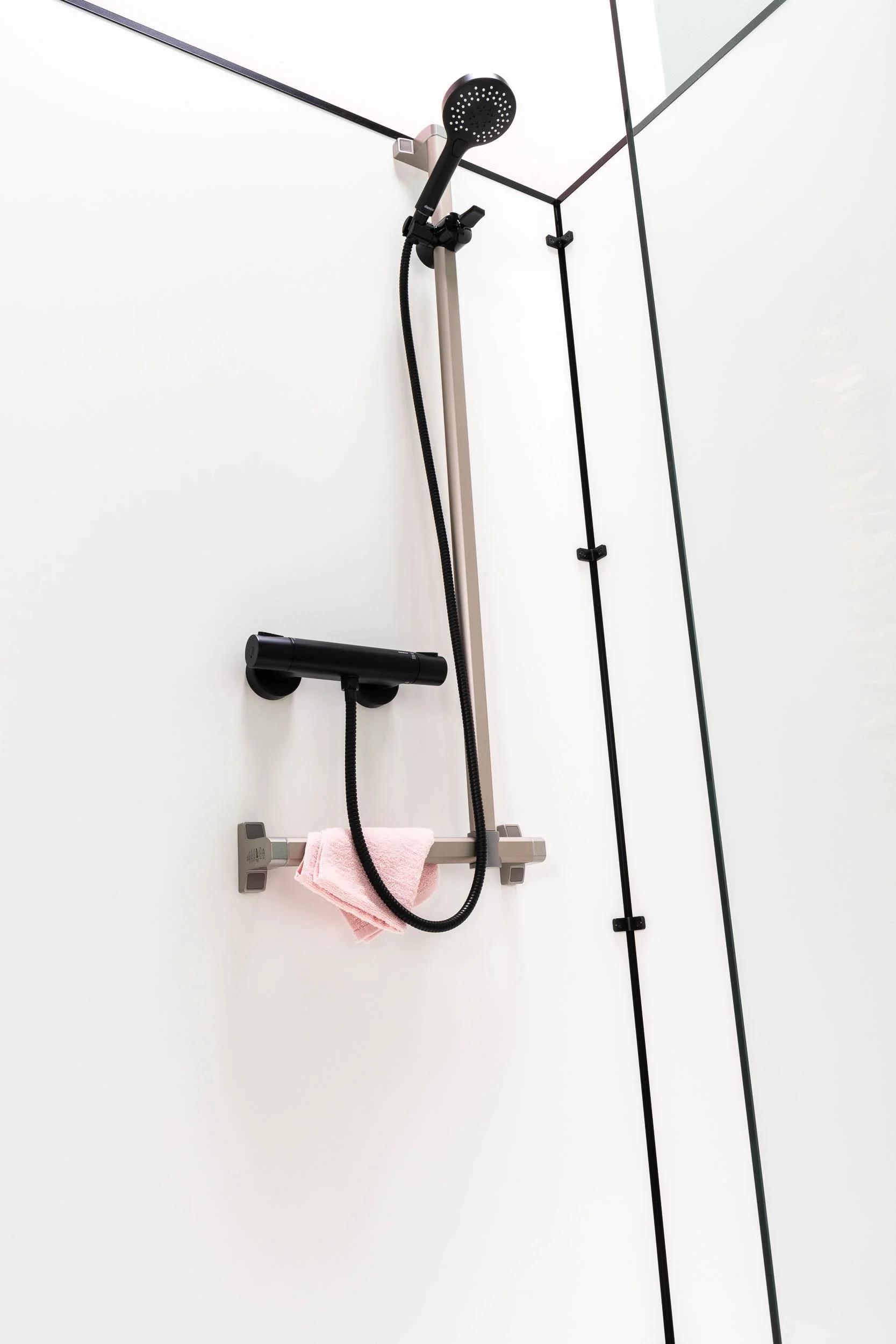 Douche moderne avec pommeau, flexible noir et support de rangement avec une serviette rose.