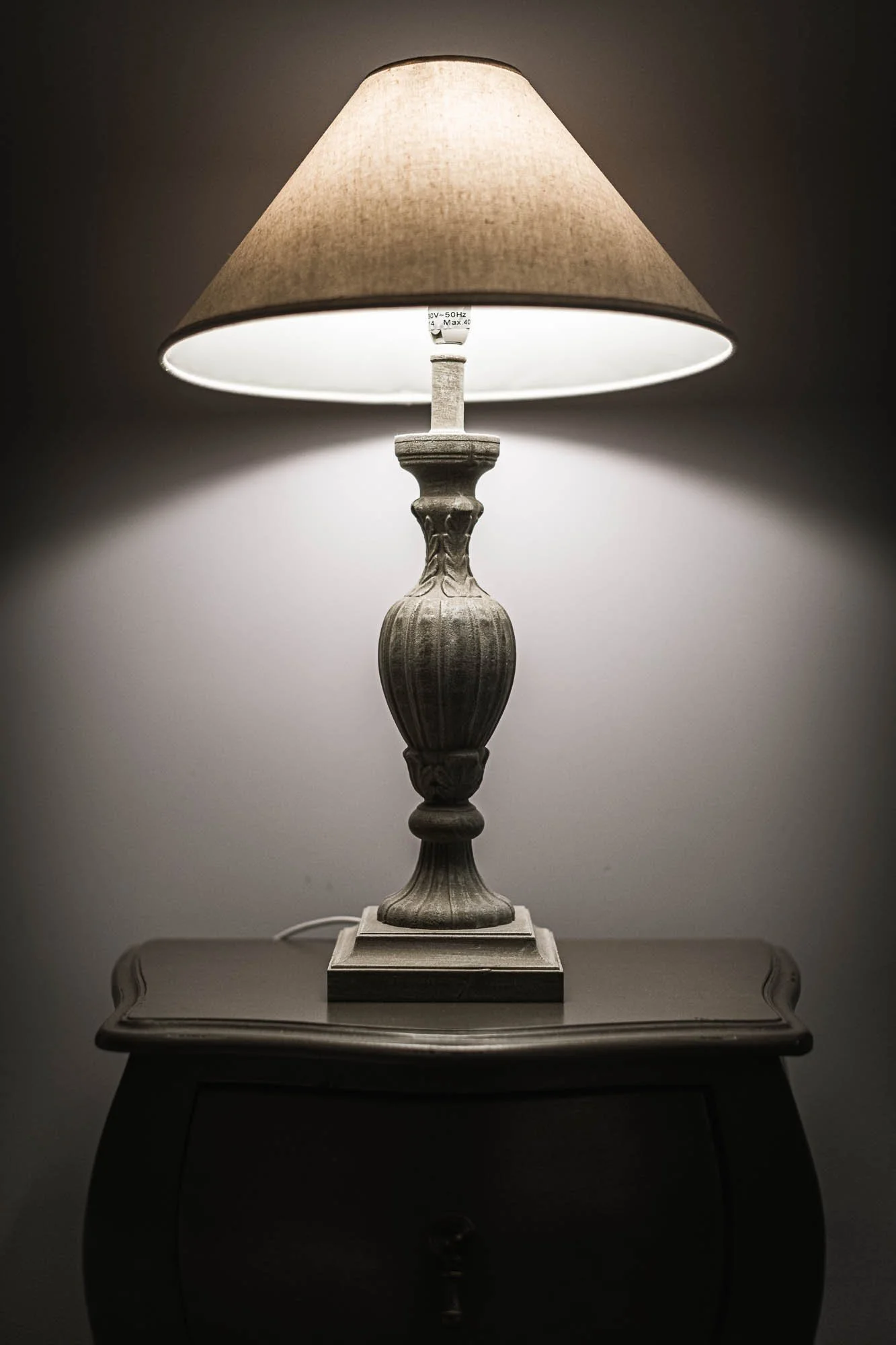Lampe de table avec un abat-jour beige sur une commode grise.
