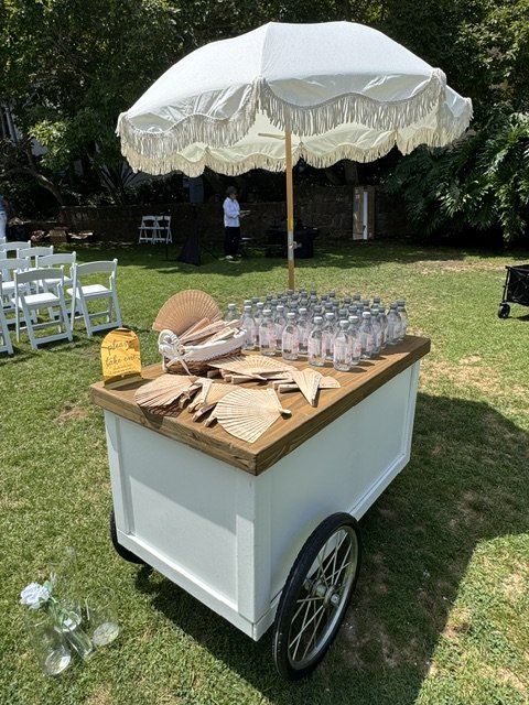 Mobile snack cart used as a guest welcome wagon holding water and fans for wedding guests.