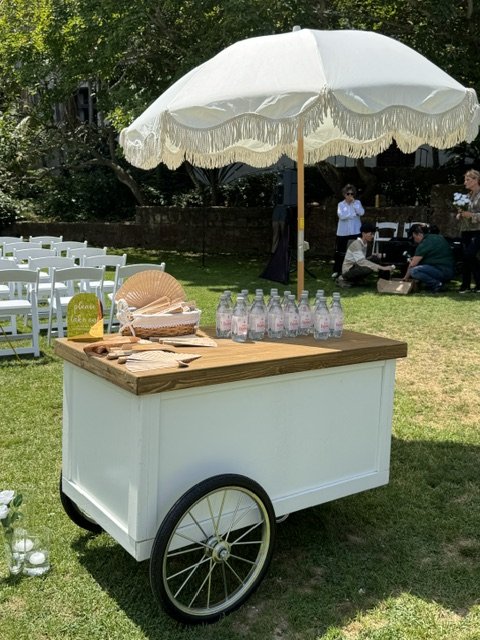 Mobile snack cart used as a guest welcome wagon holding water and fans for wedding guests.