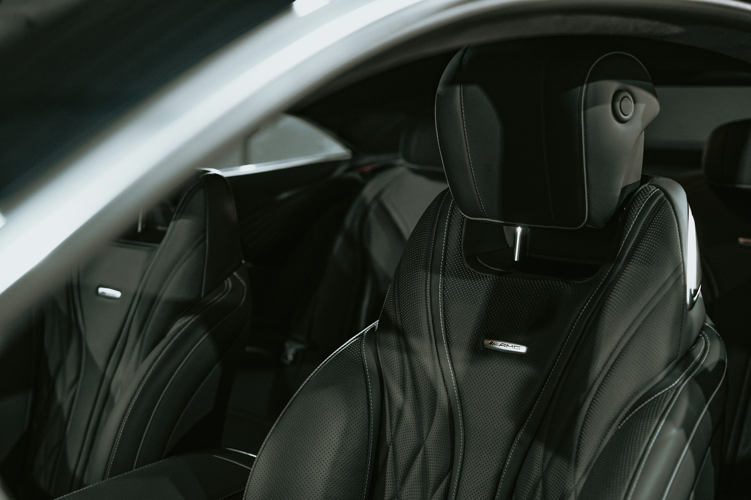 Luxury car interior with black leather seat featuring AMG branding, headrest, and stitching details.