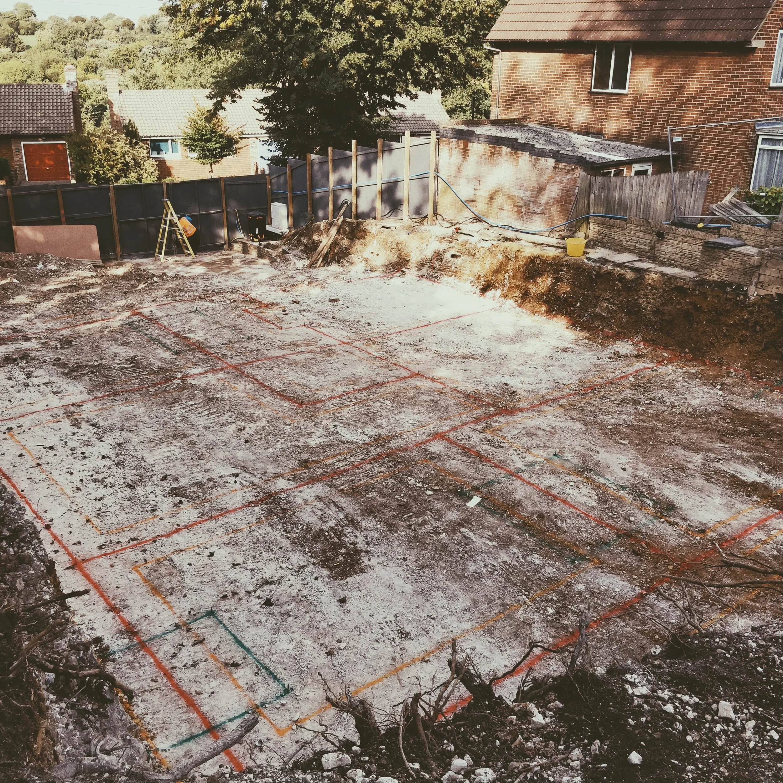 Construction site with marked-out foundation for building, surrounded by residential houses and trees.