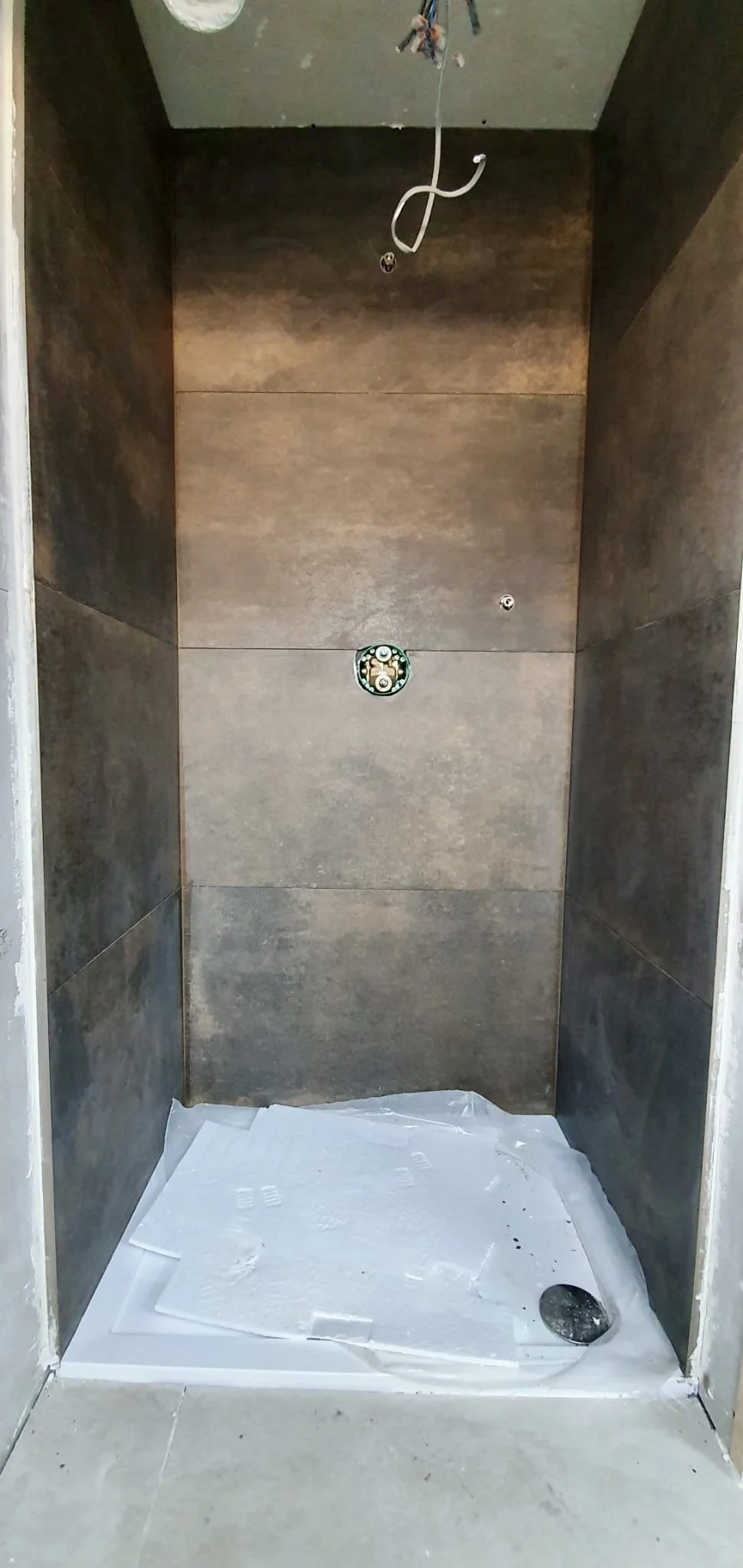 Empty shower stall with brown tiled walls, a circular drain on the white shower base, and exposed wiring hanging from the ceiling.